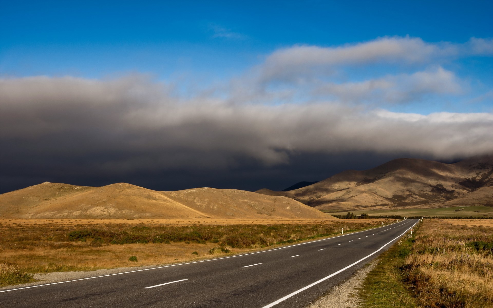 Road through rolling hills under cloudy sky HD Wallpaper