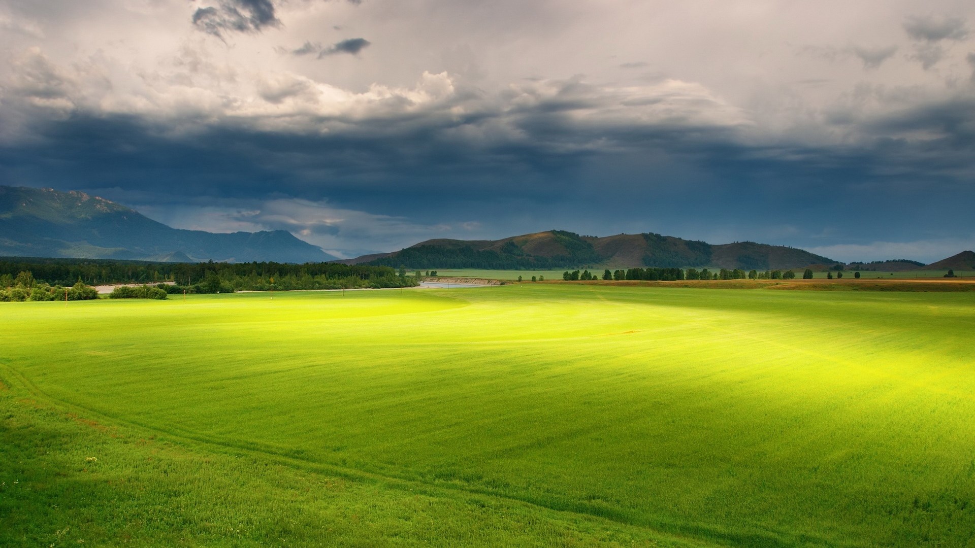 Green field with mountains and stormy clouds HD Wallpaper