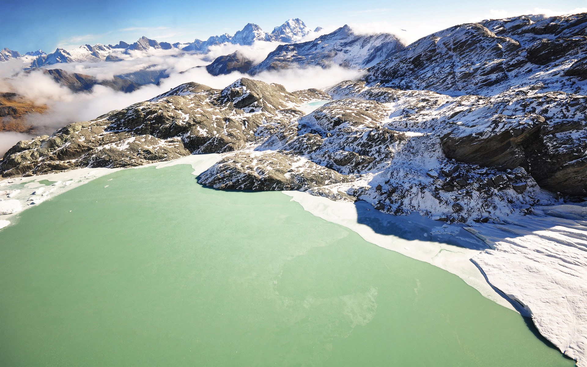 Turquoise glacial lake surrounded by snow-capped mountains HD Wallpaper