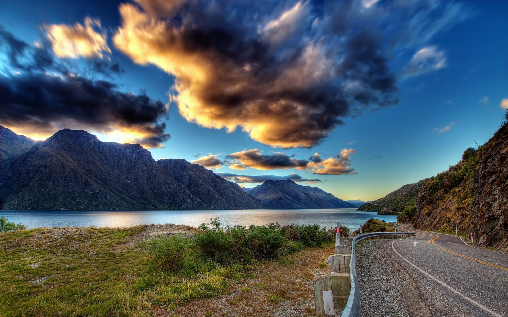 Mountain lake with winding road and dramatic clouds HD Wallpaper