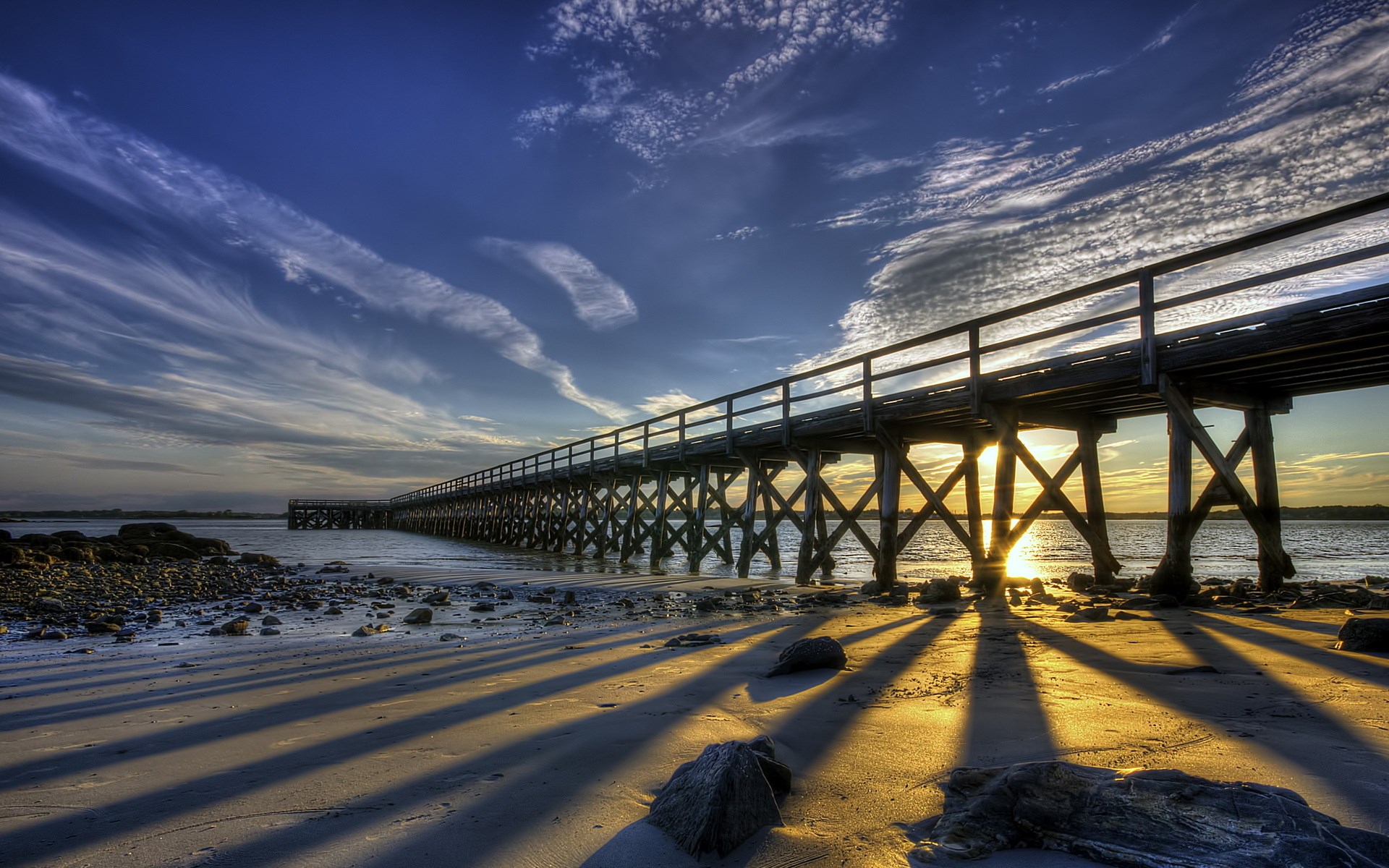 Wooden pier casting long shadows on a beach at sunset HD Wallpaper