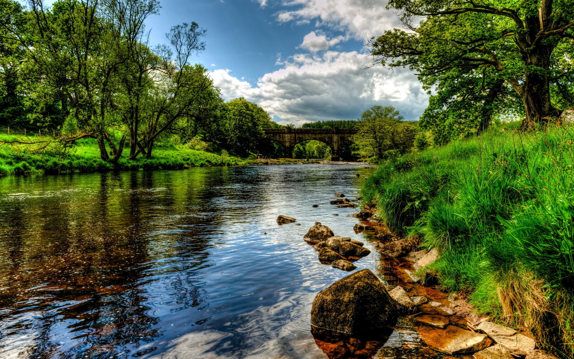 River flowing under an arched stone bridge surrounded by trees HD Wallpaper