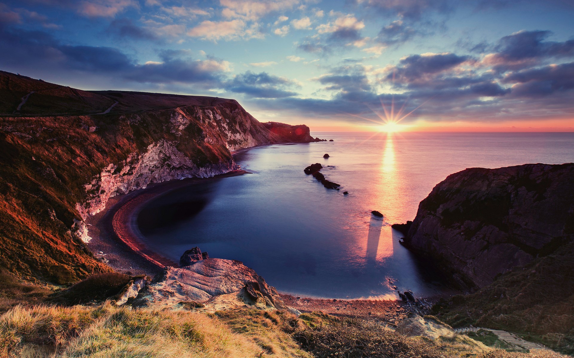 Sunrise over a rocky coastline and calm sea HD Wallpaper