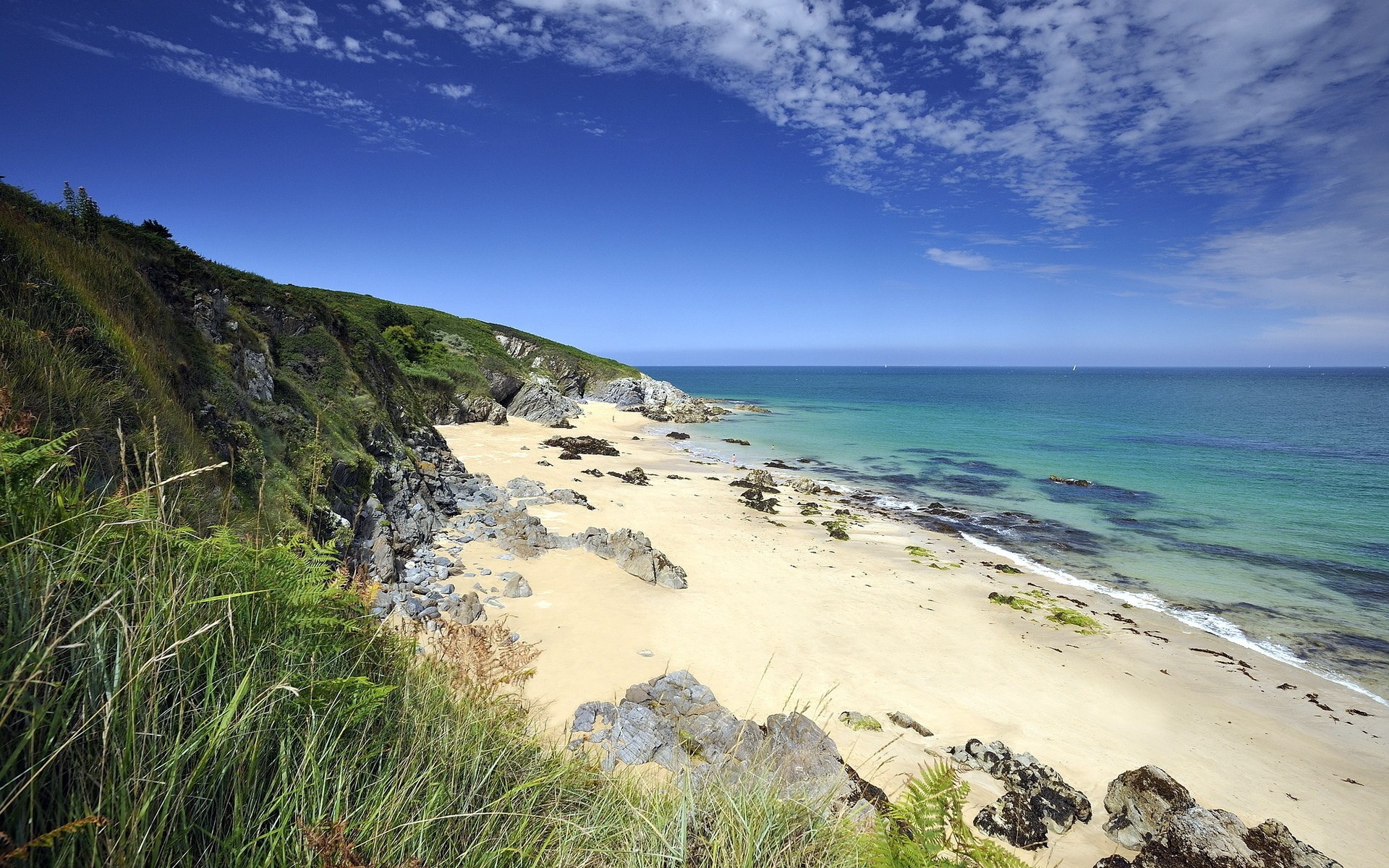 Sandy beach with rocky cliffs and turquoise ocean under blue sky HD Wallpaper