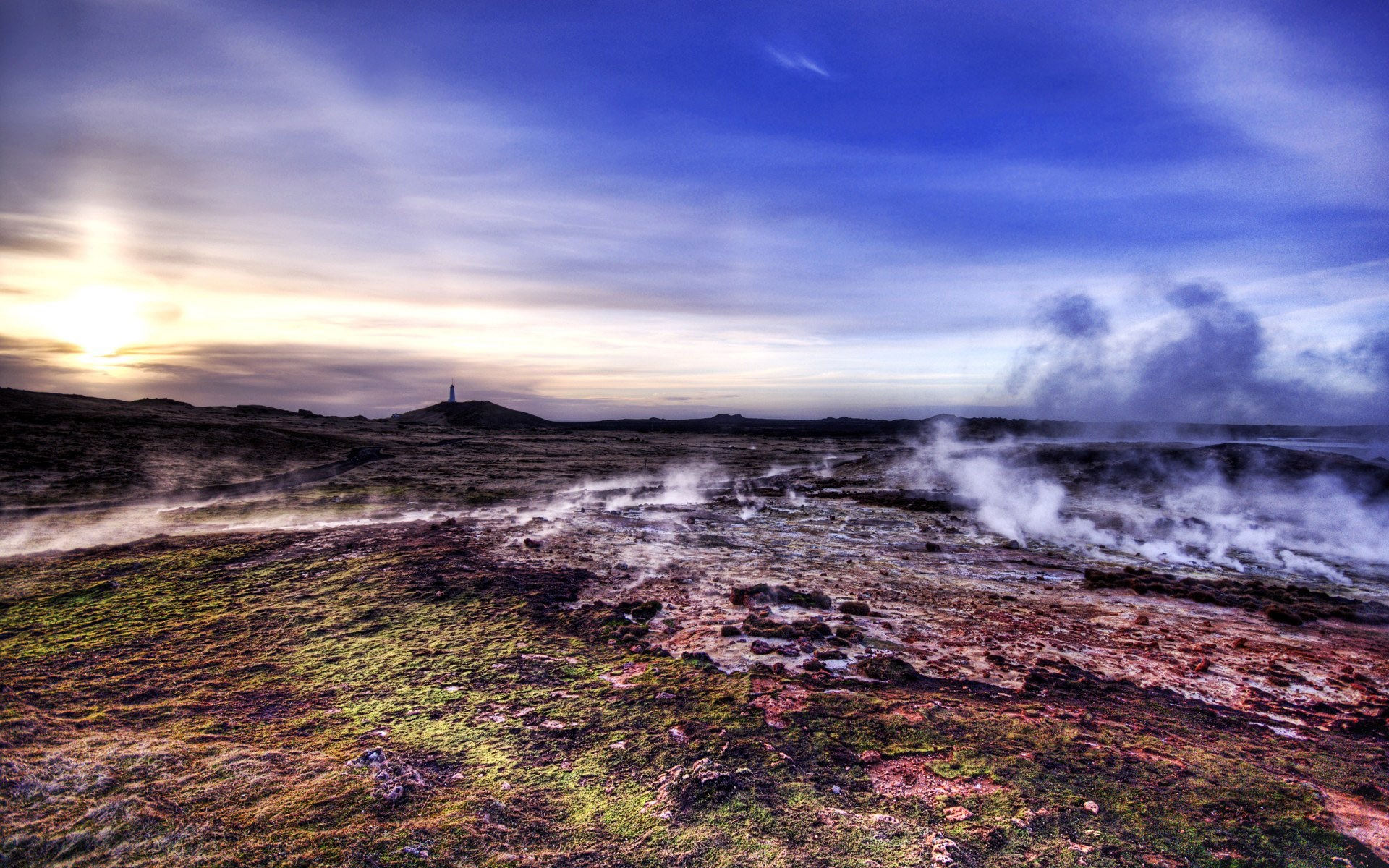 Geothermal landscape with steam and a distant lighthouse HD Wallpaper