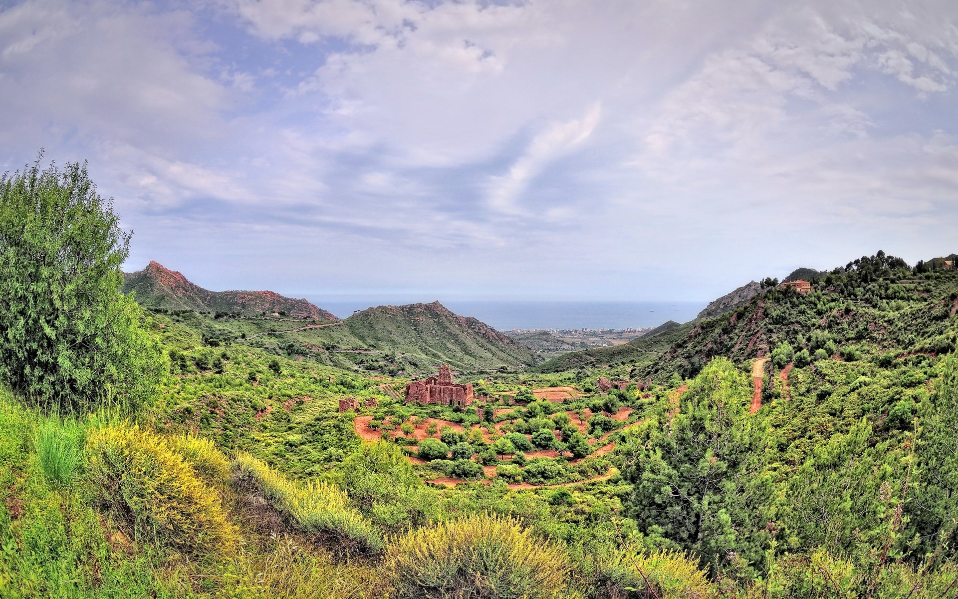 Ruined building in a green valley with mountains and the sea HD Wallpaper