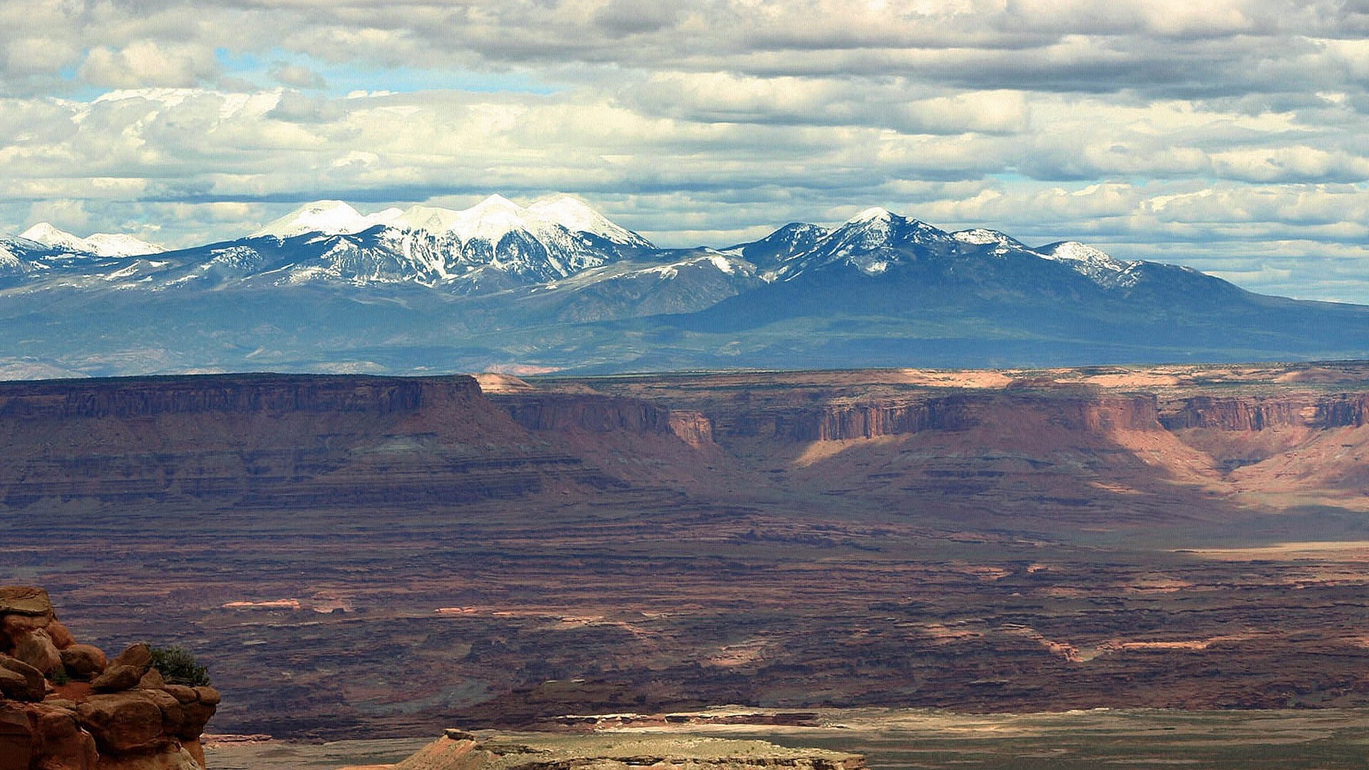 Snow-capped mountains over a desert canyon landscape HD Wallpaper