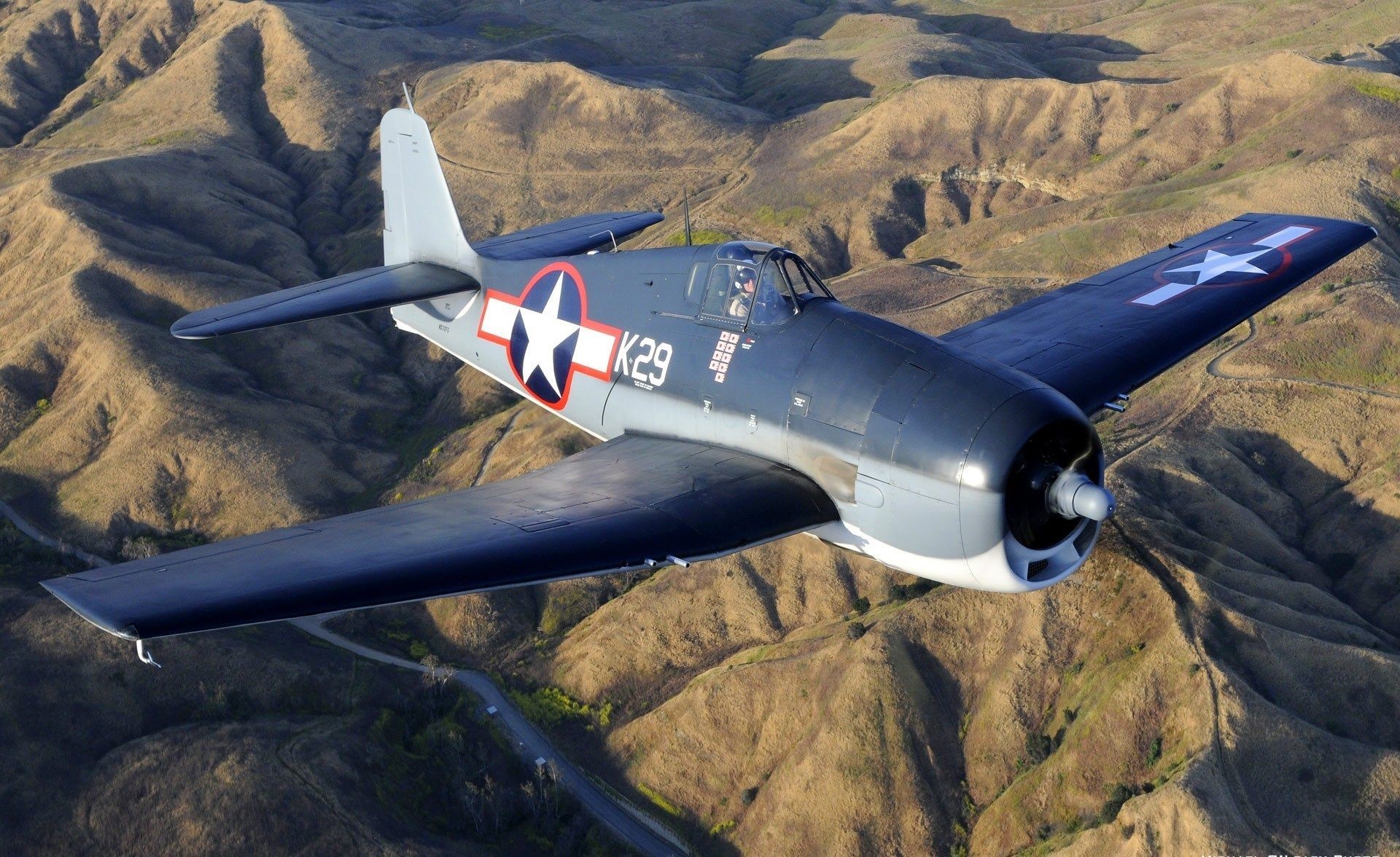 Grumman F6F Hellcat fighter plane flying over hills HD Wallpaper
