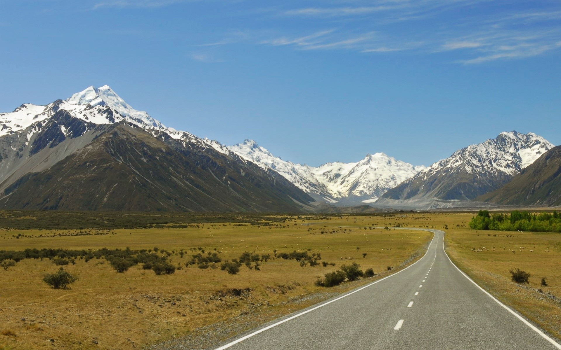 Road leading to snow-capped mountains under a blue sky HD Wallpaper