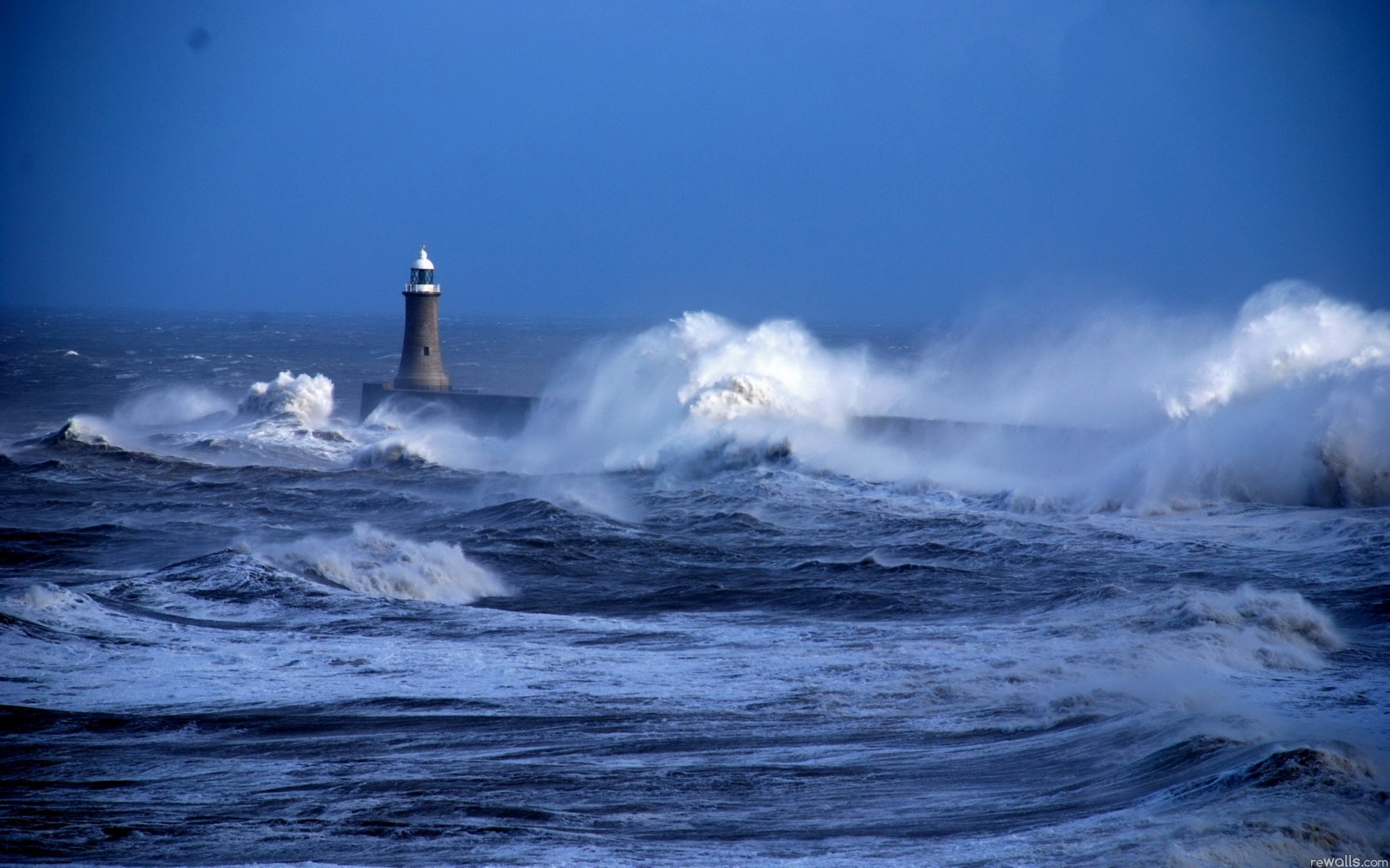 Stormy seas crash against a lighthouse pier HD Wallpaper