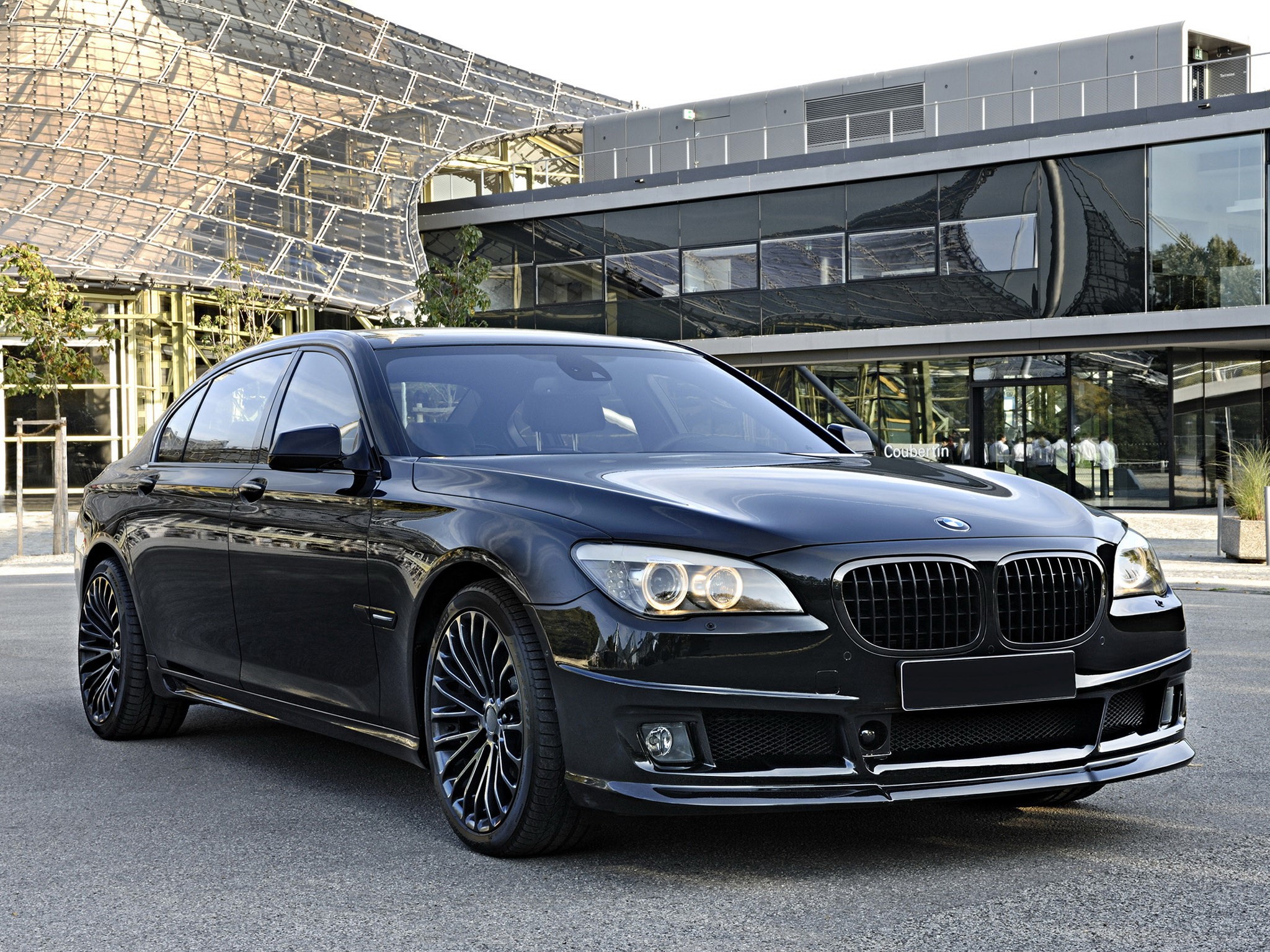 Black BMW 7 Series Sedan in front of modern architecture HD Wallpaper
