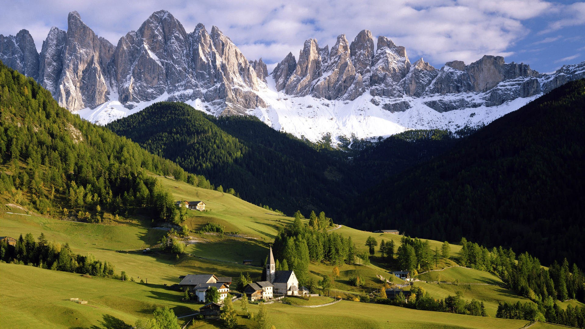 Snow-capped mountains above a green valley with a village HD Wallpaper