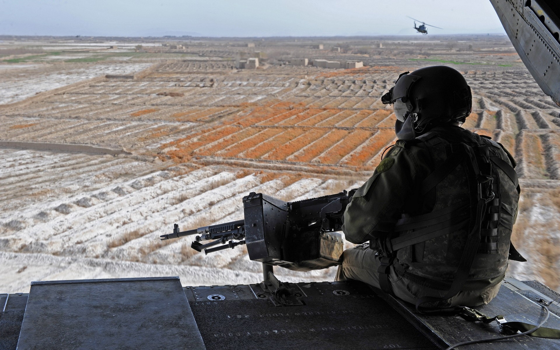 Soldier with machine gun in helicopter overlooking farmland HD Wallpaper