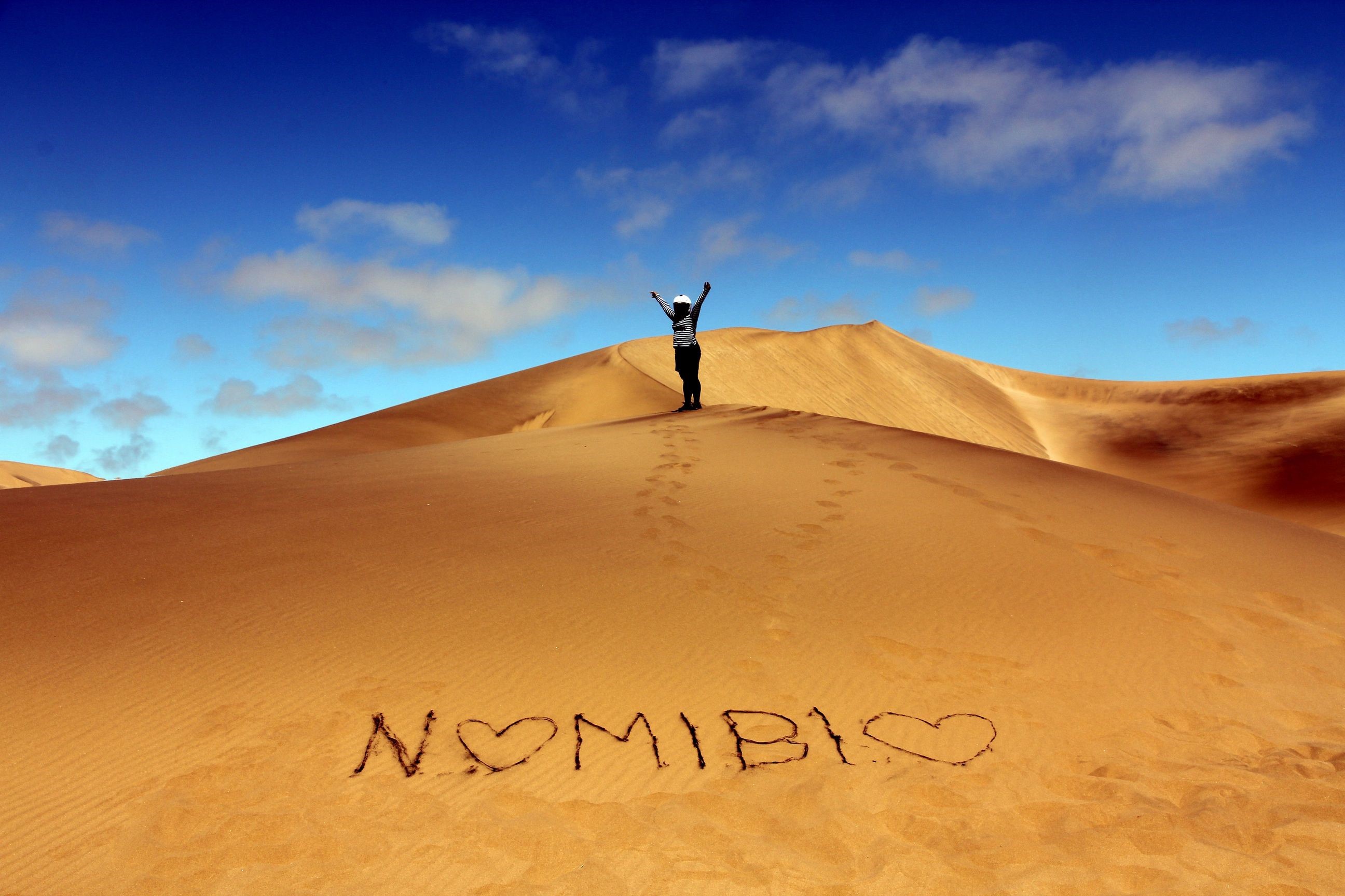 Person on sand dune with "NAMIBIA" written in sand HD Wallpaper