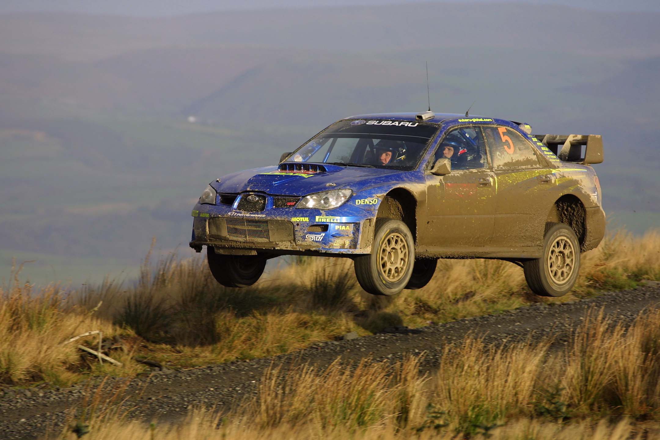 Subaru rally car jumping over a dirt track HD Wallpaper
