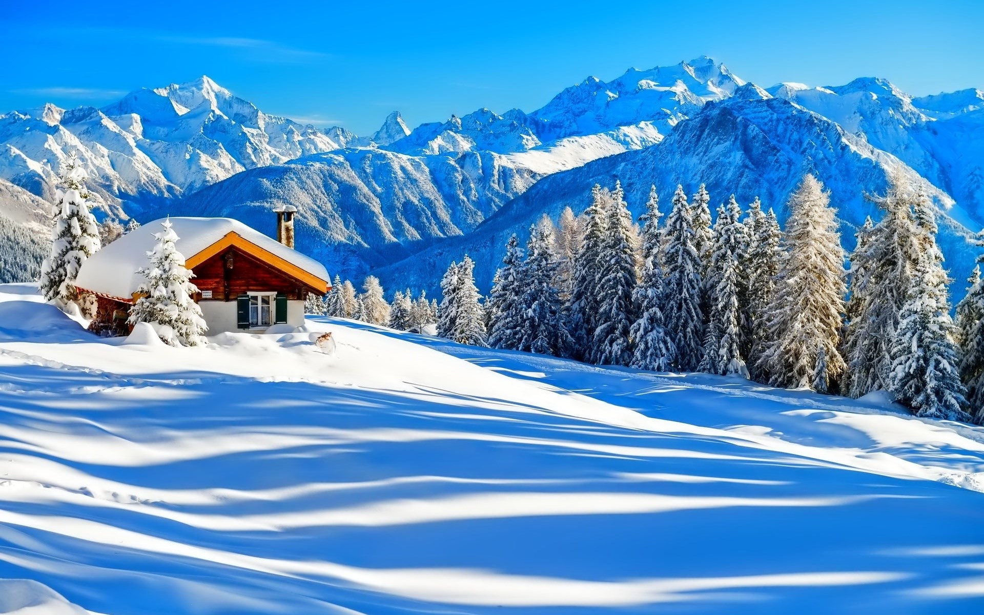 Snowy cabin in the Alps with snow-covered trees and mountains HD Wallpaper