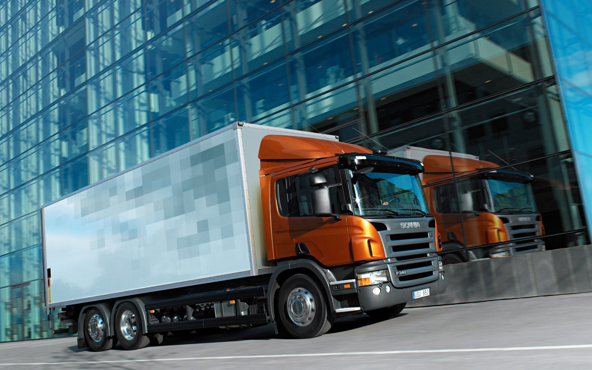 Two Scania trucks driving past a modern glass building HD Wallpaper