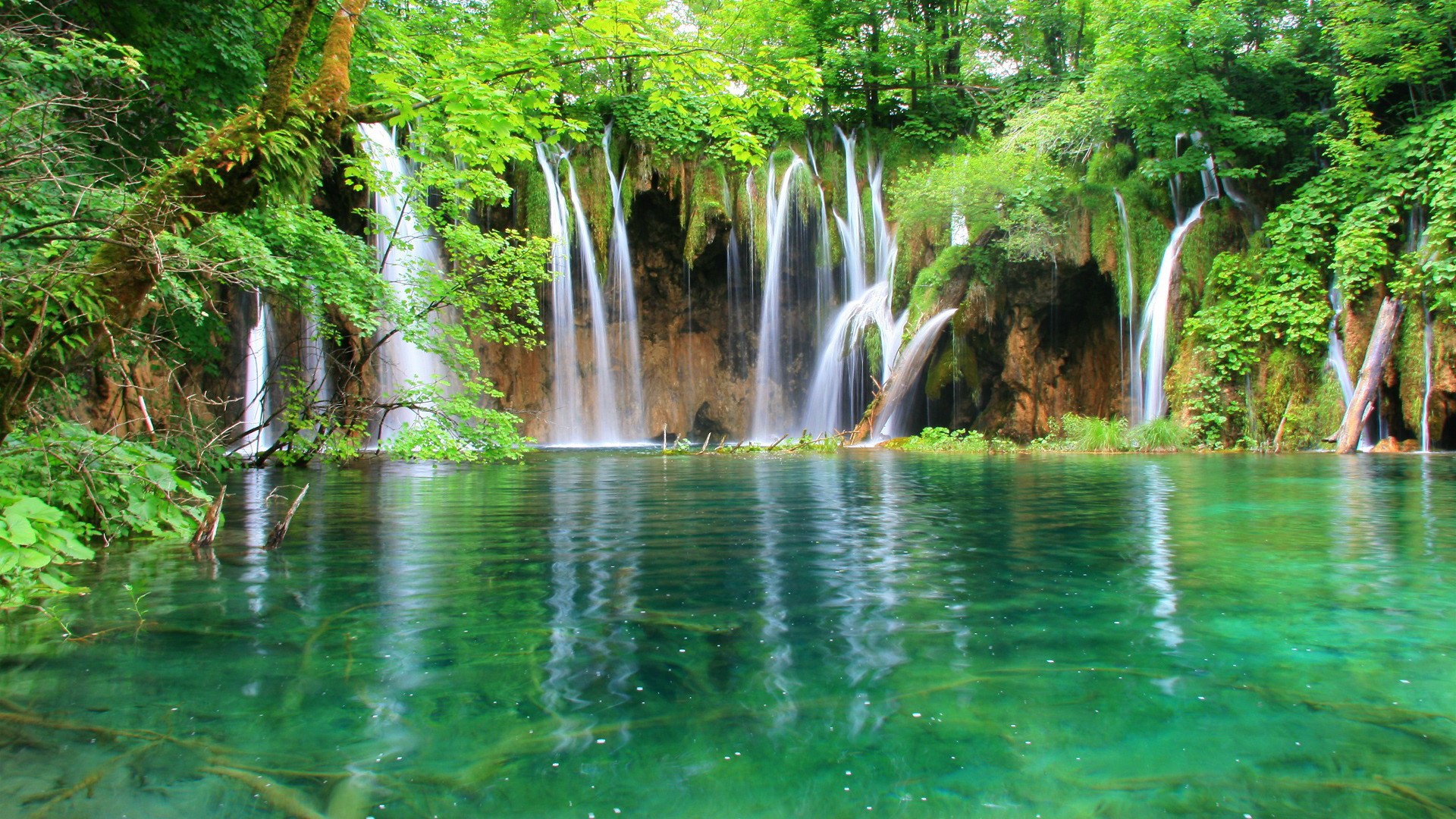 Waterfalls cascading into a clear green lake HD Wallpaper