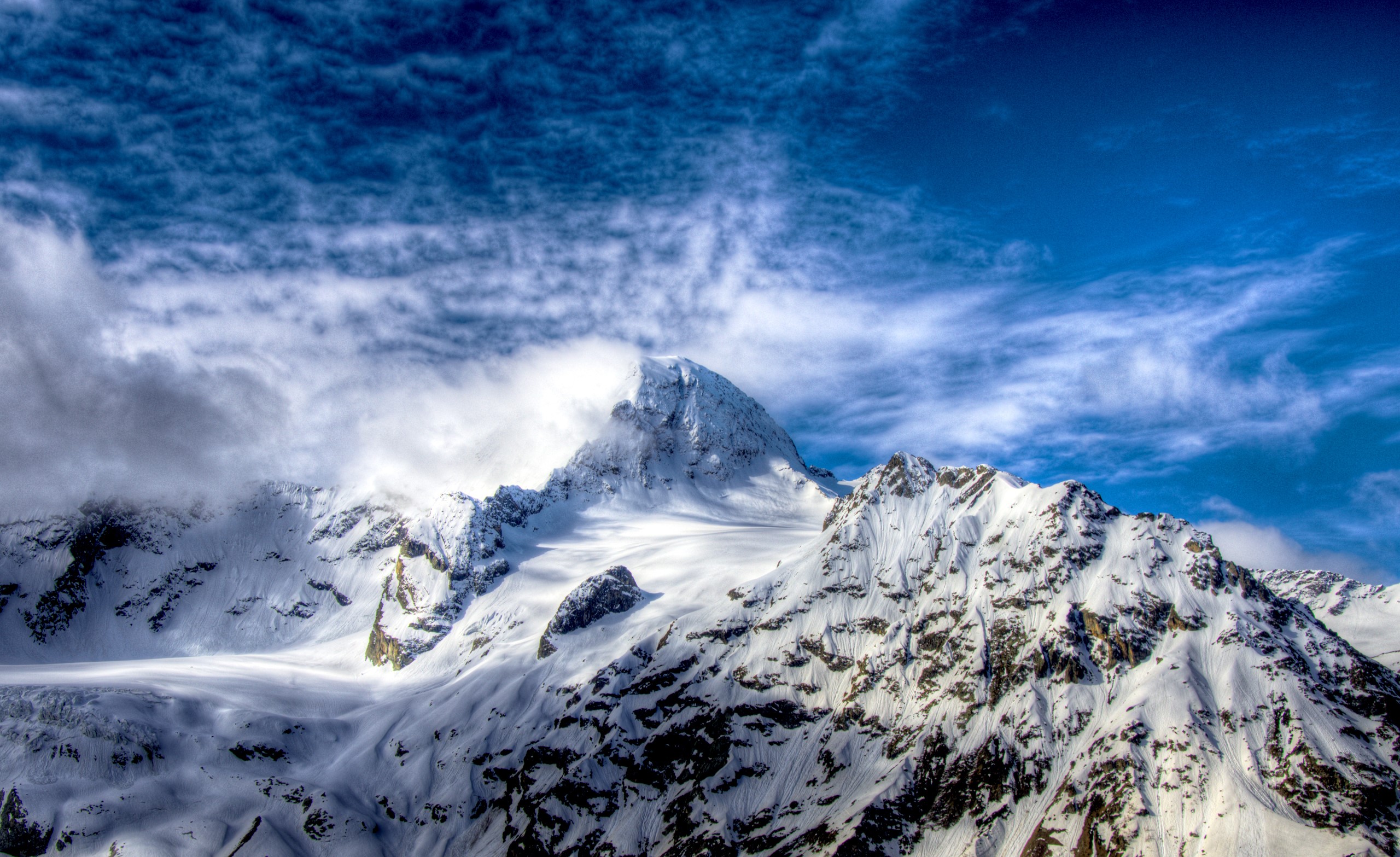 Snow-covered mountains under a cloudy blue sky HD Wallpaper
