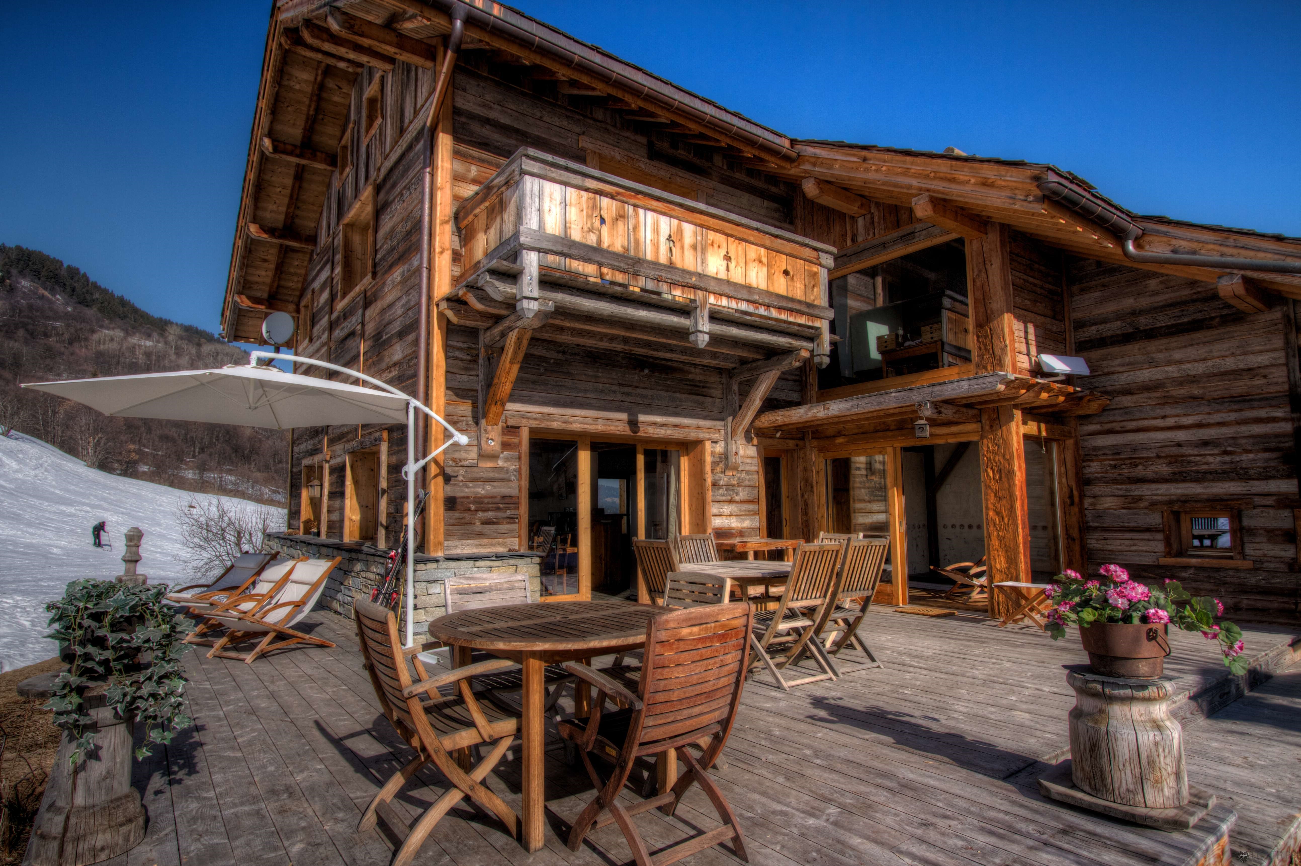 Wooden Chalet with Outdoor Seating and Snowy Mountains HD Wallpaper