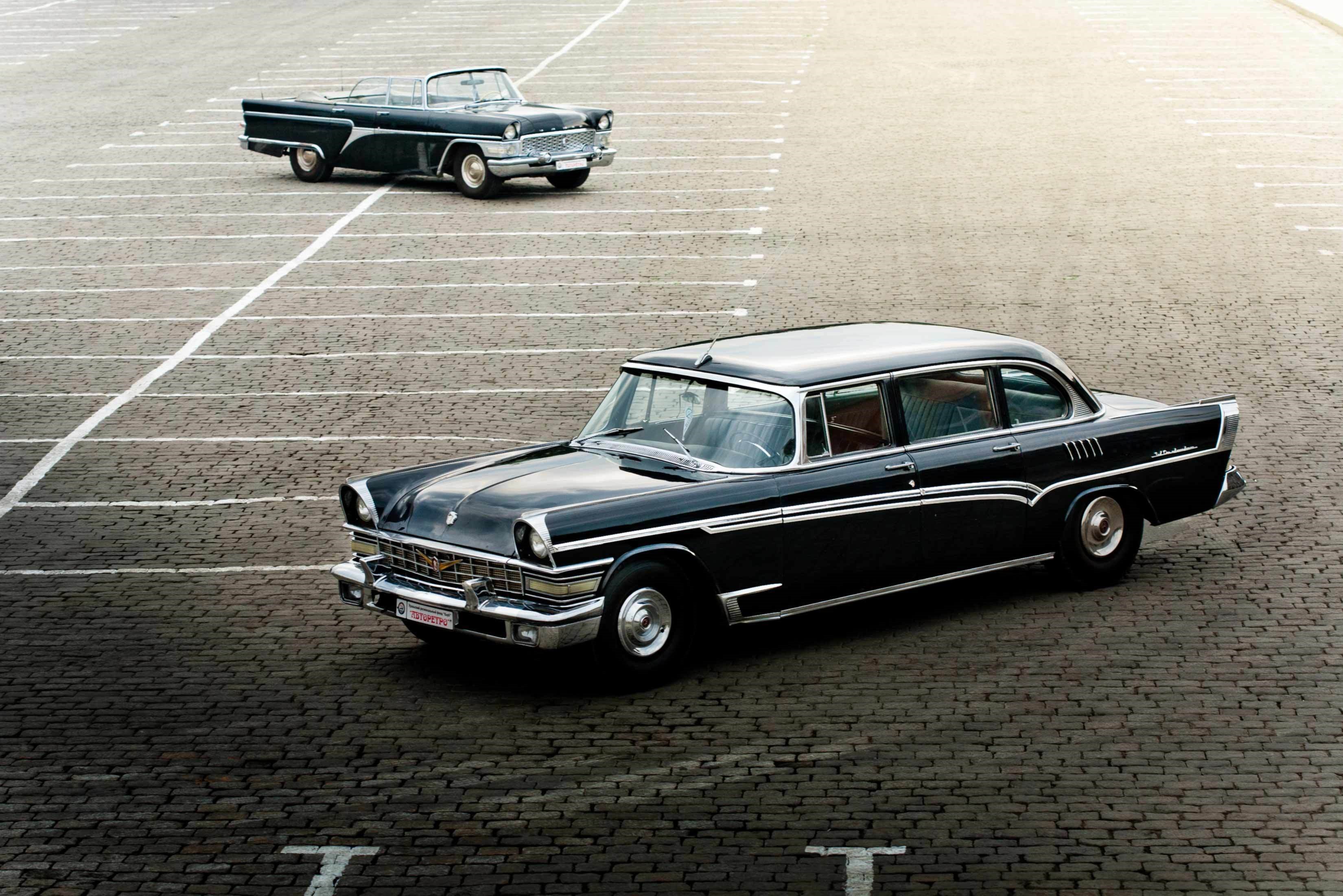Two vintage black GAZ-13 Chaika cars parked on cobblestone HD Wallpaper
