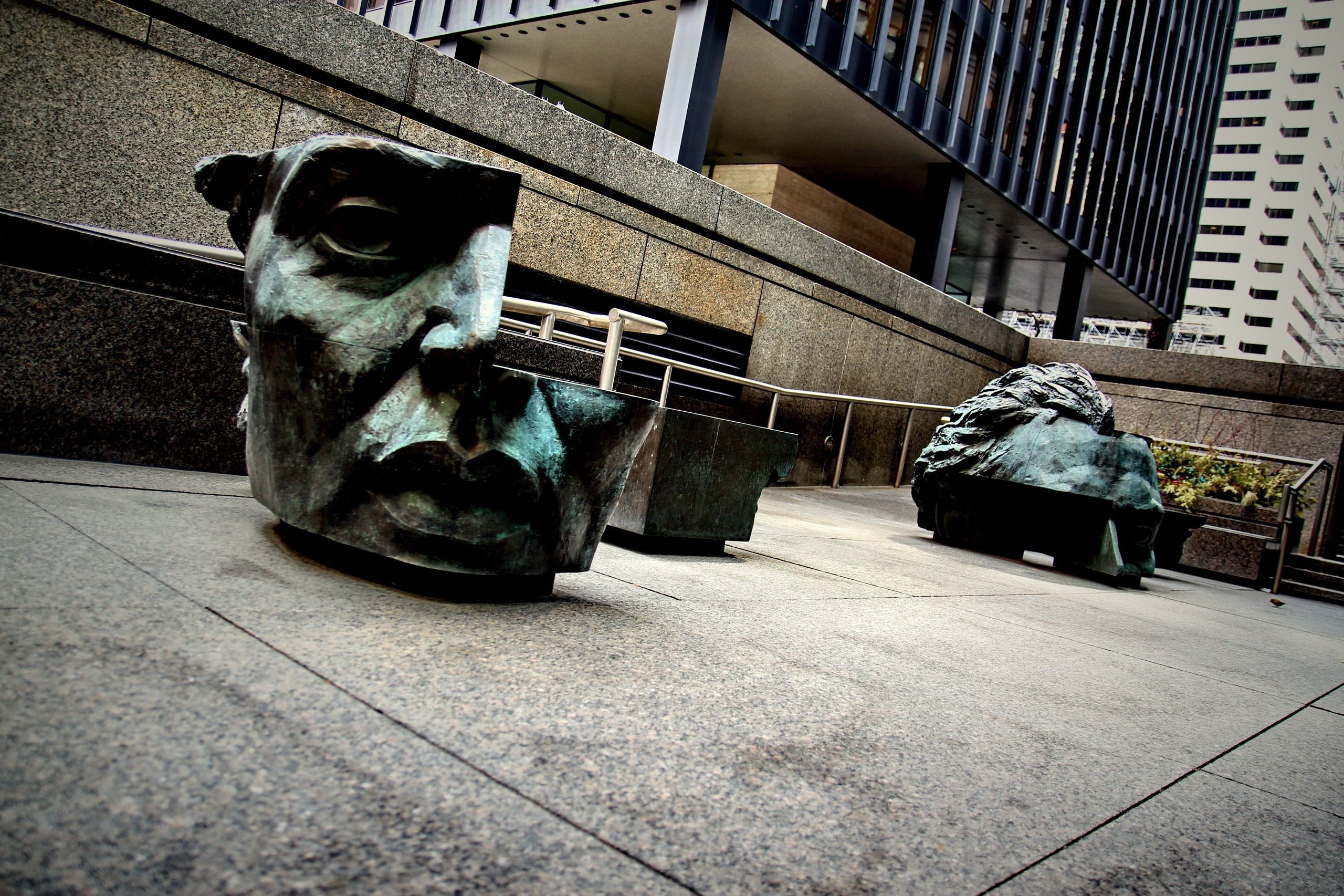 Sculptures of faces in a city plaza HD Wallpaper