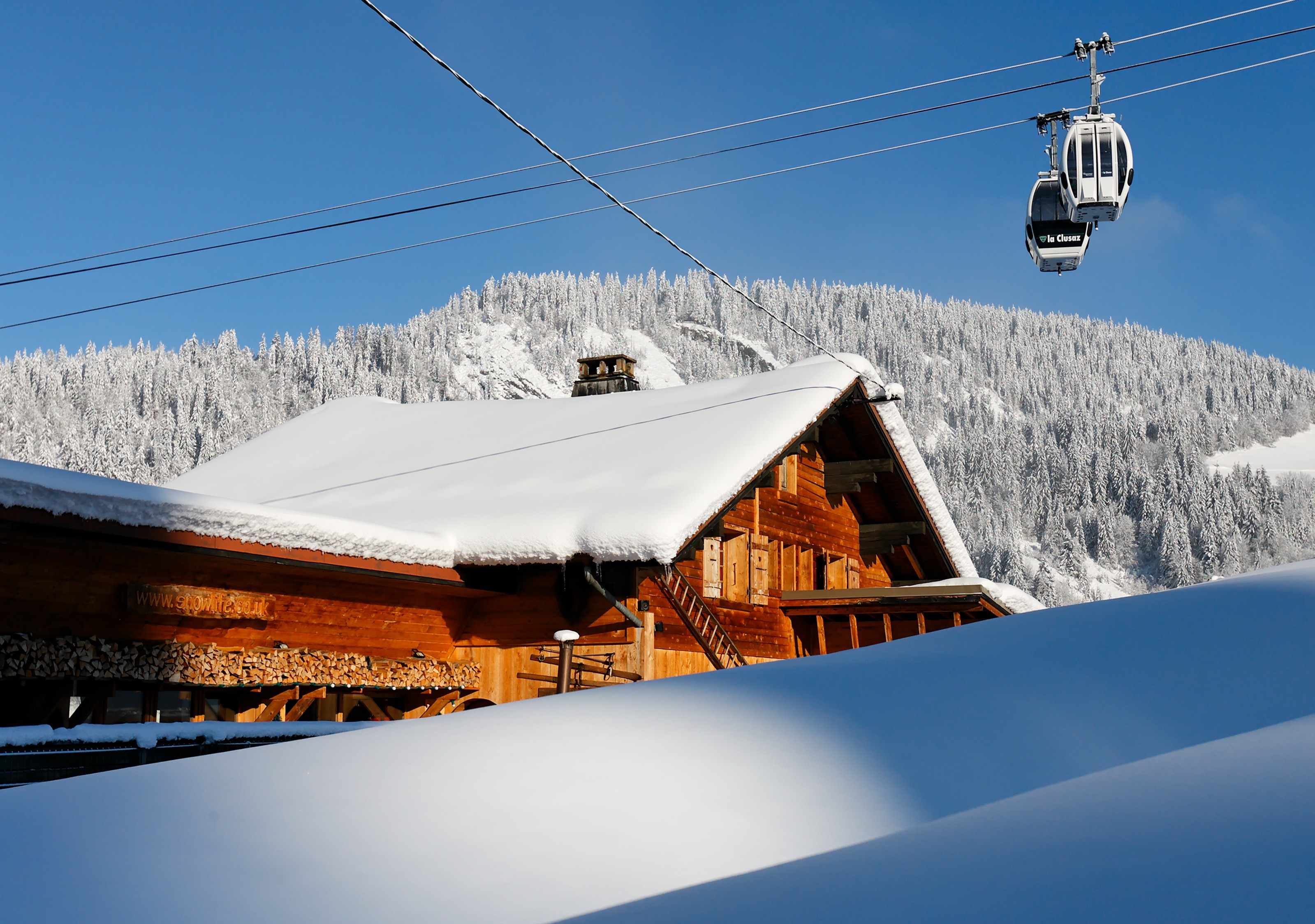 Wooden chalet with snow-covered roof and ski lift HD Wallpaper
