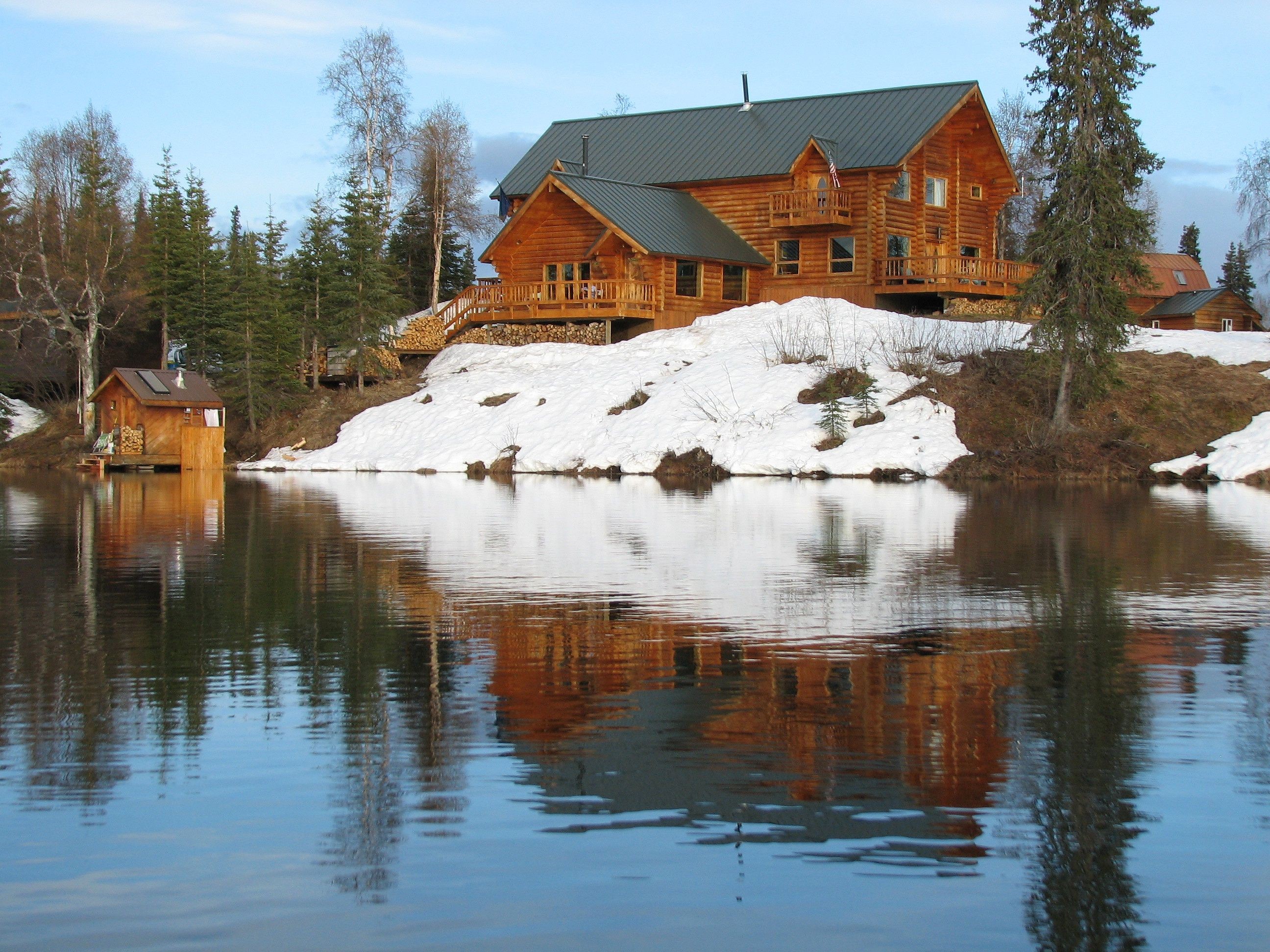 Log cabin on a snowy hill overlooking a lake in the USA HD Wallpaper