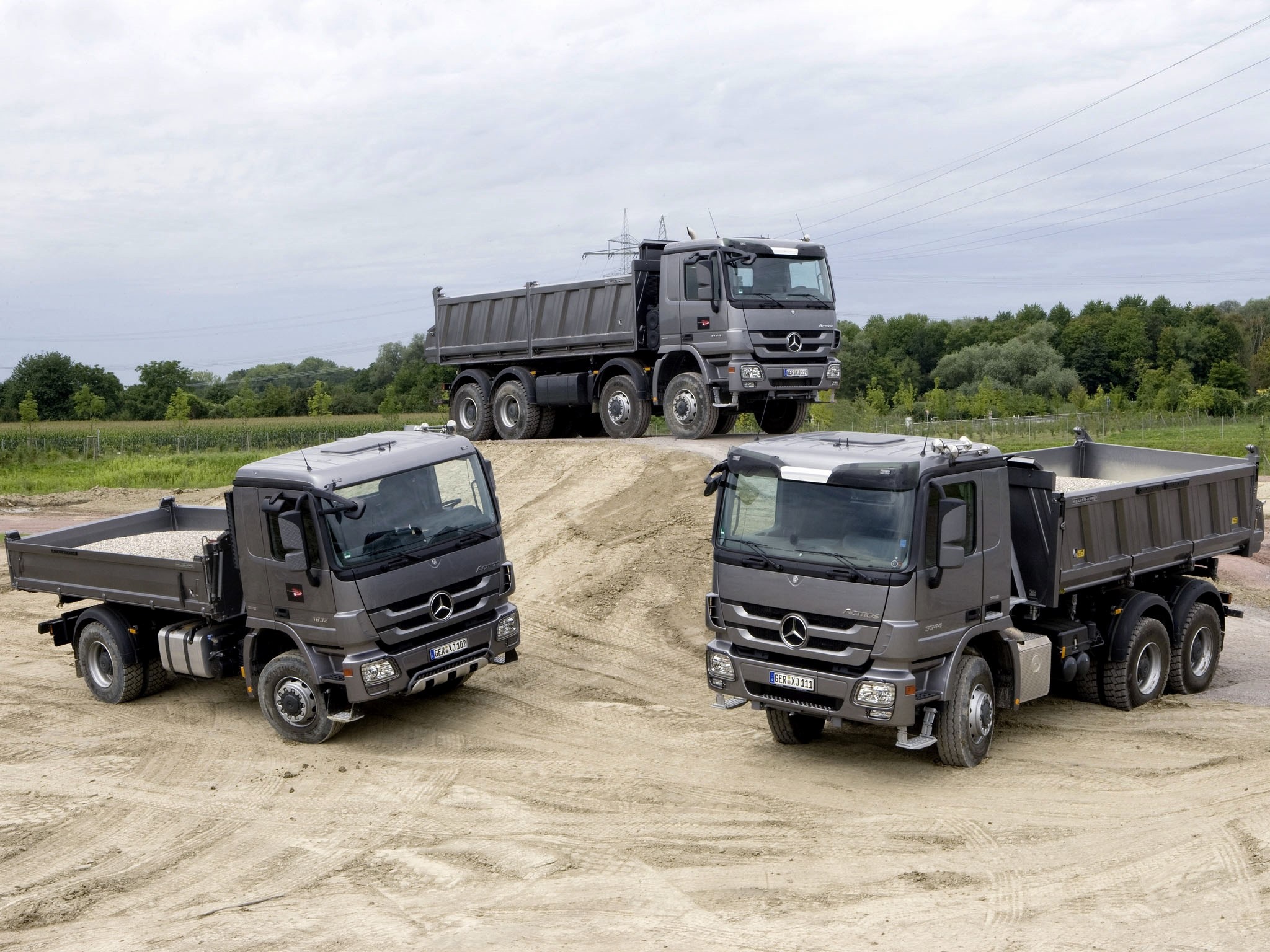 Three Mercedes-Benz dump trucks on a dirt pile HD Wallpaper