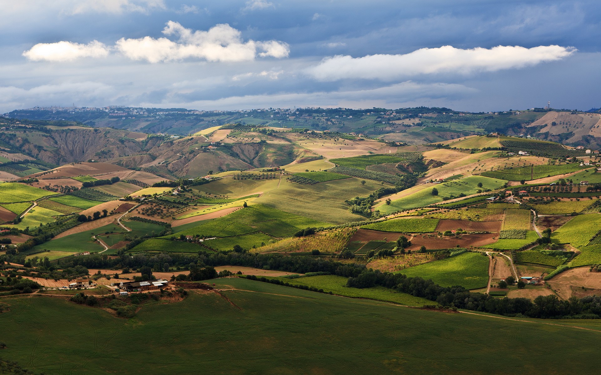 Rolling hills with agricultural fields under a cloudy sky HD Wallpaper