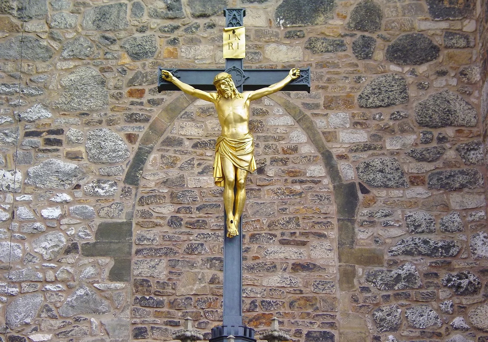 Golden Jesus Christ on a cross in front of a stone wall HD Wallpaper