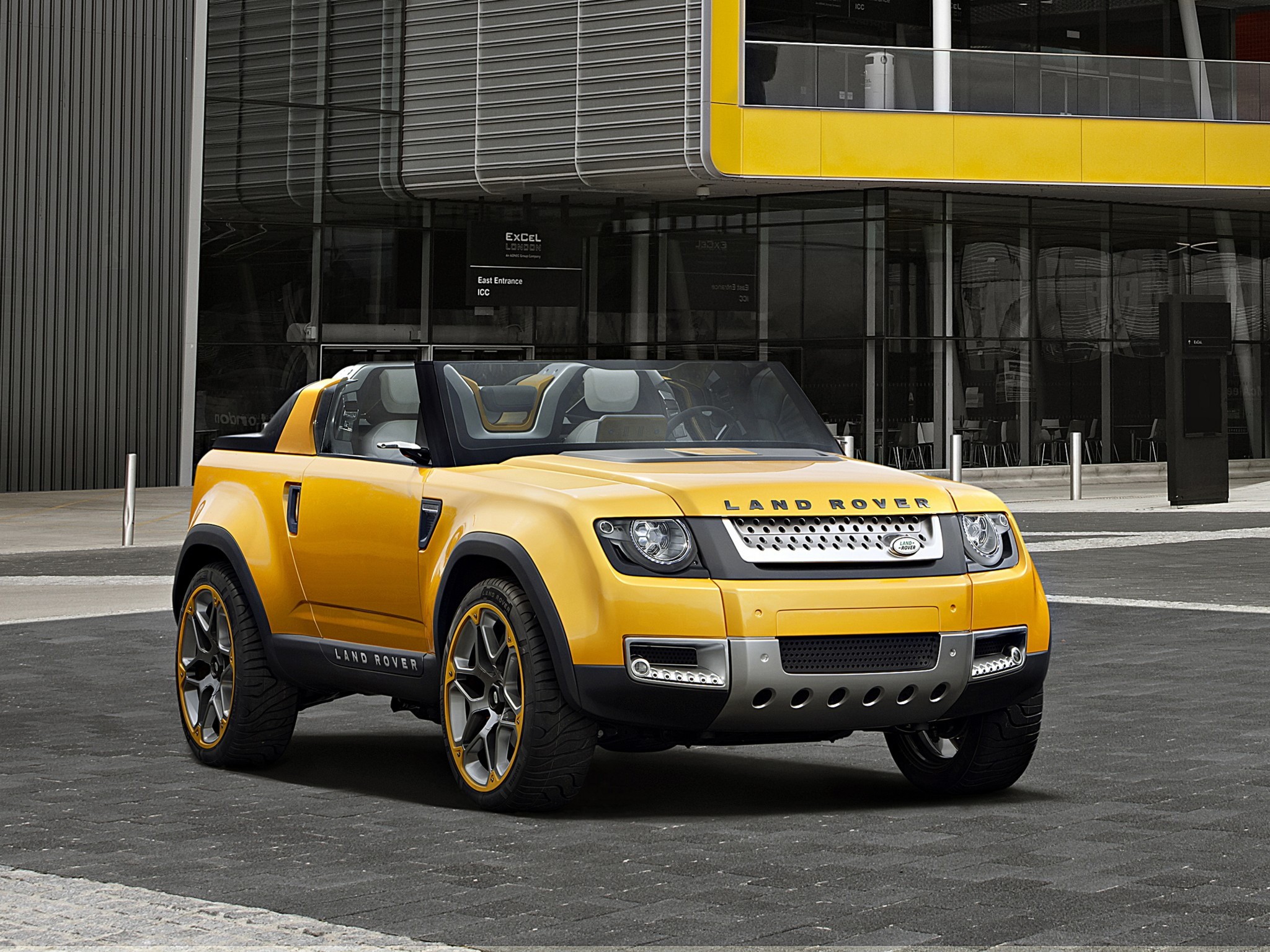 Yellow Land Rover concept car in front of modern building HD Wallpaper