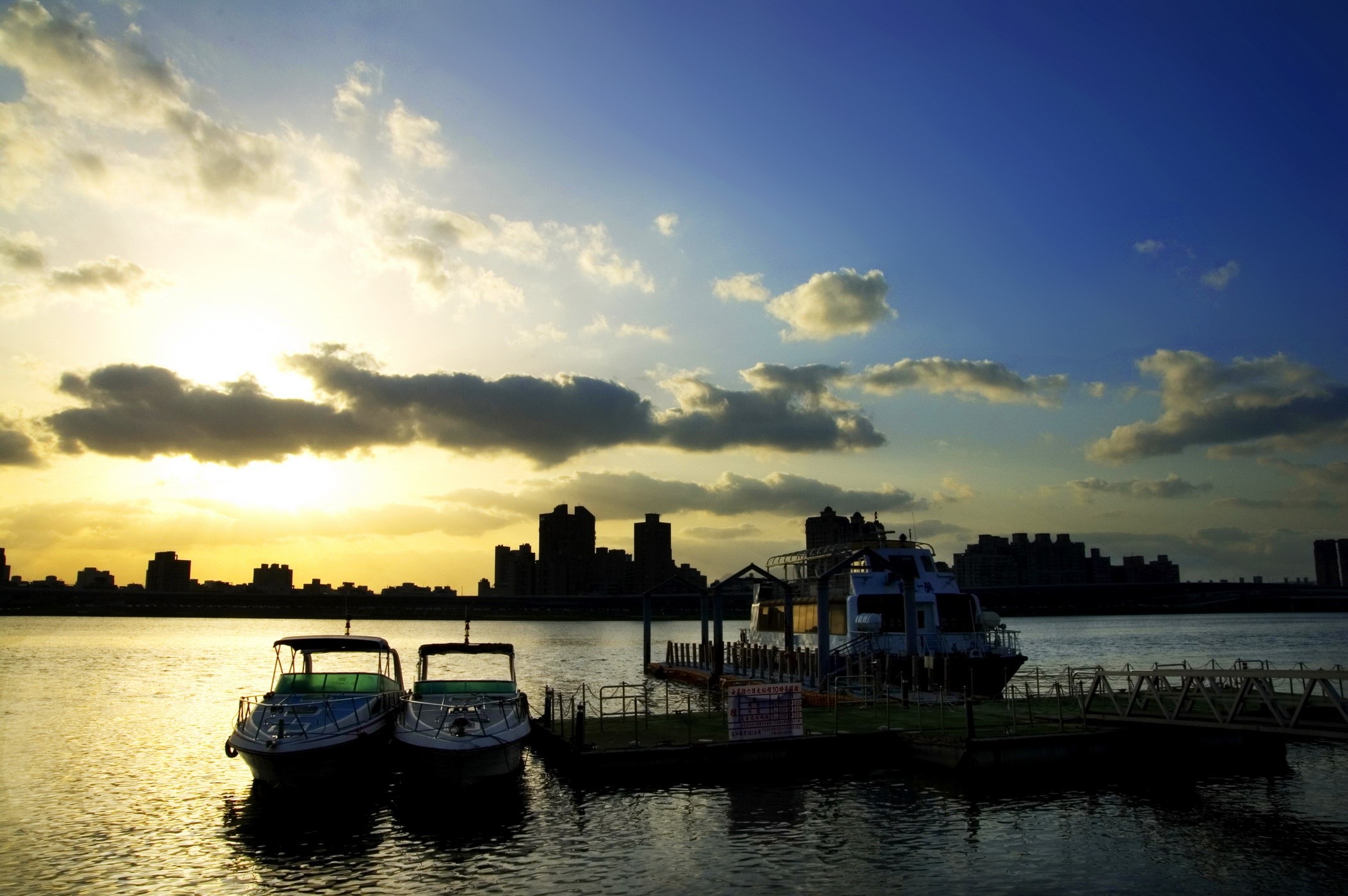 Boats docked on a river at sunset with city skyline HD Wallpaper