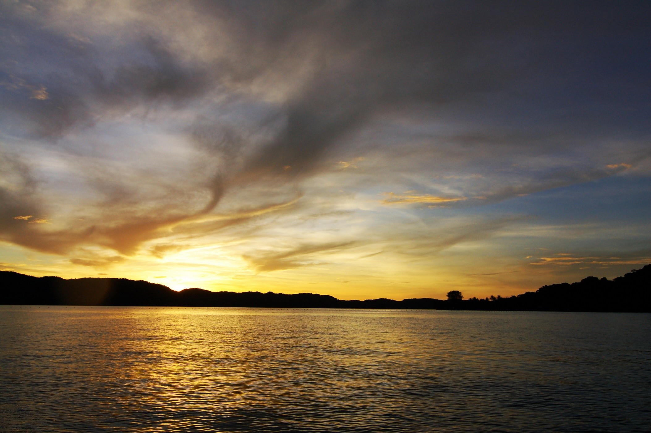 Sunset over a calm body of water with silhouetted hills HD Wallpaper