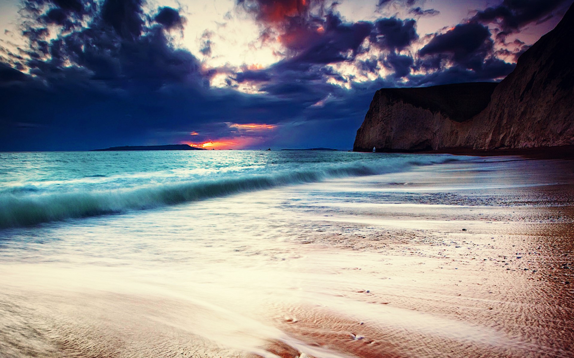 Dramatic sunset over a rocky coastline and ocean waves HD Wallpaper