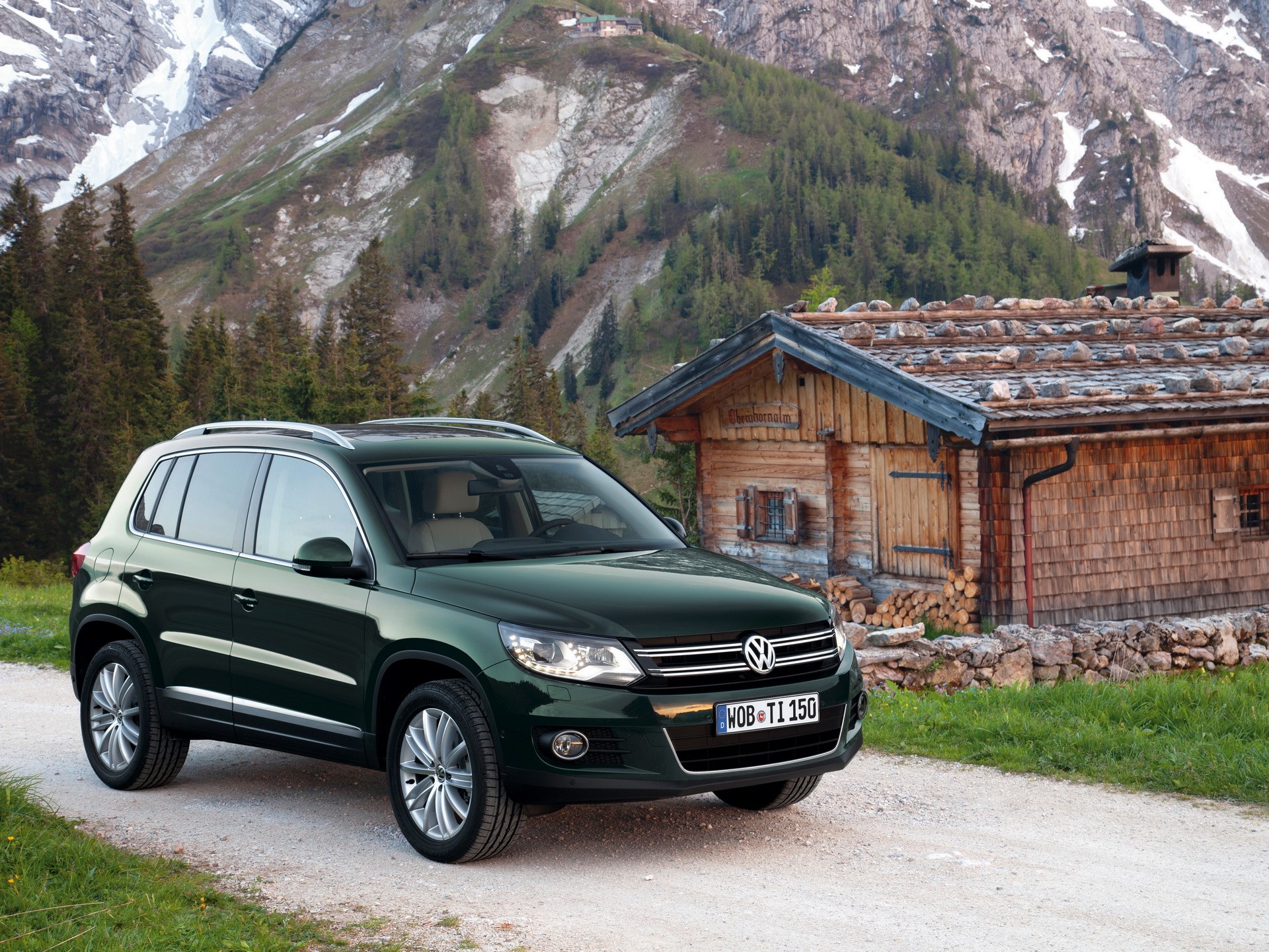 Green Volkswagen Tiguan parked near a wooden cabin in the mountains HD Wallpaper