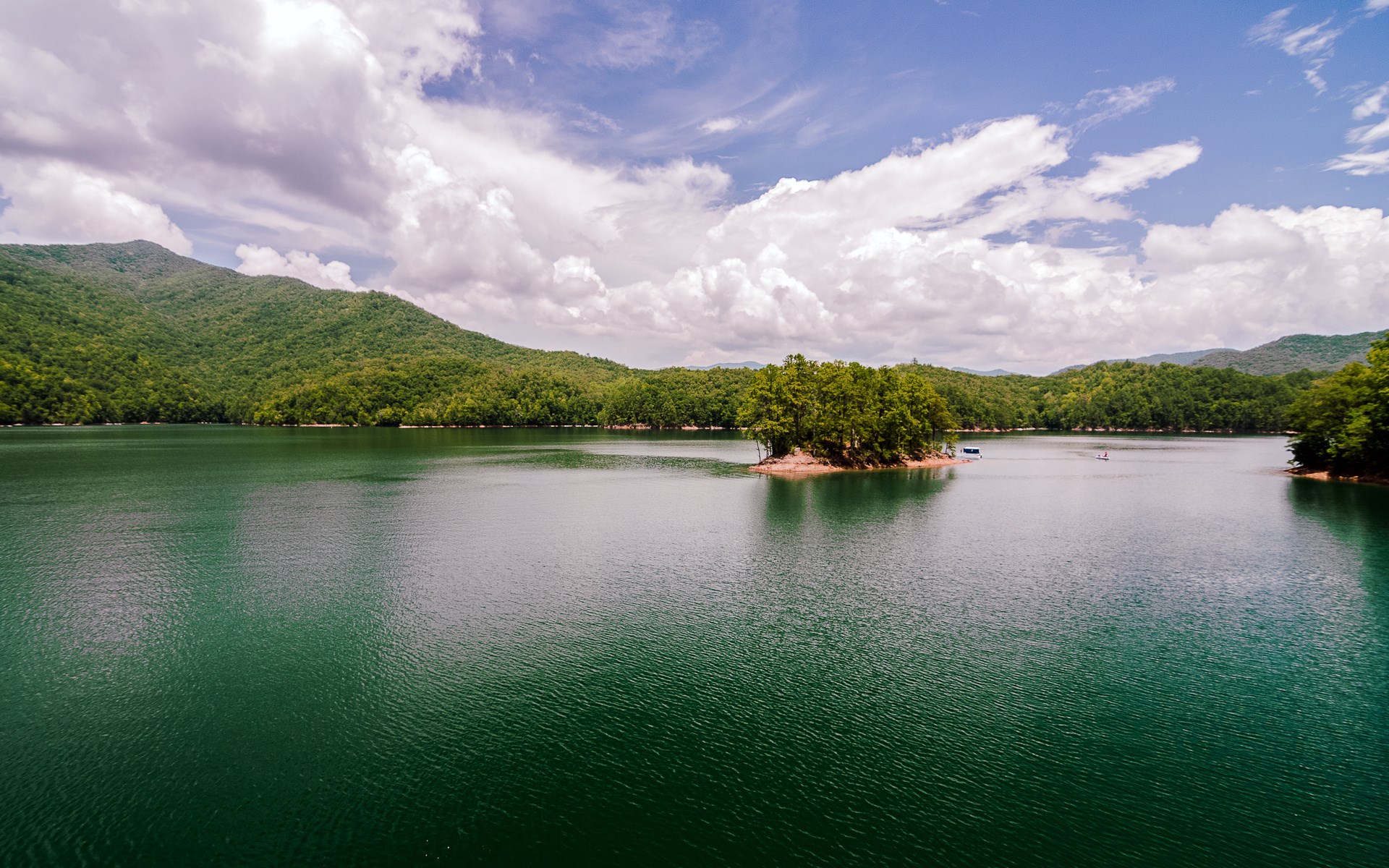Lake surrounded by green mountains under a cloudy sky HD Wallpaper