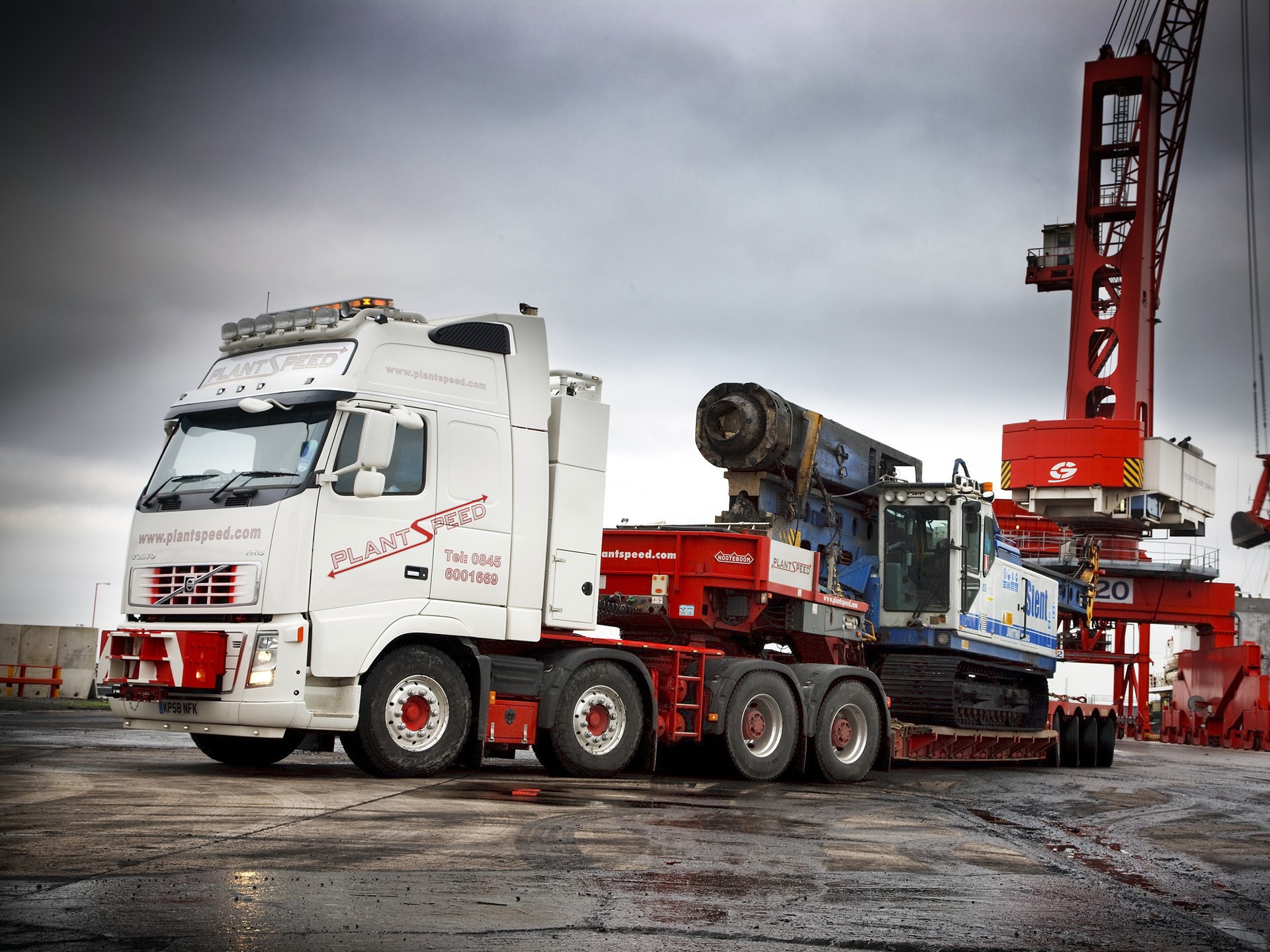Volvo truck carrying heavy machinery at a port HD Wallpaper