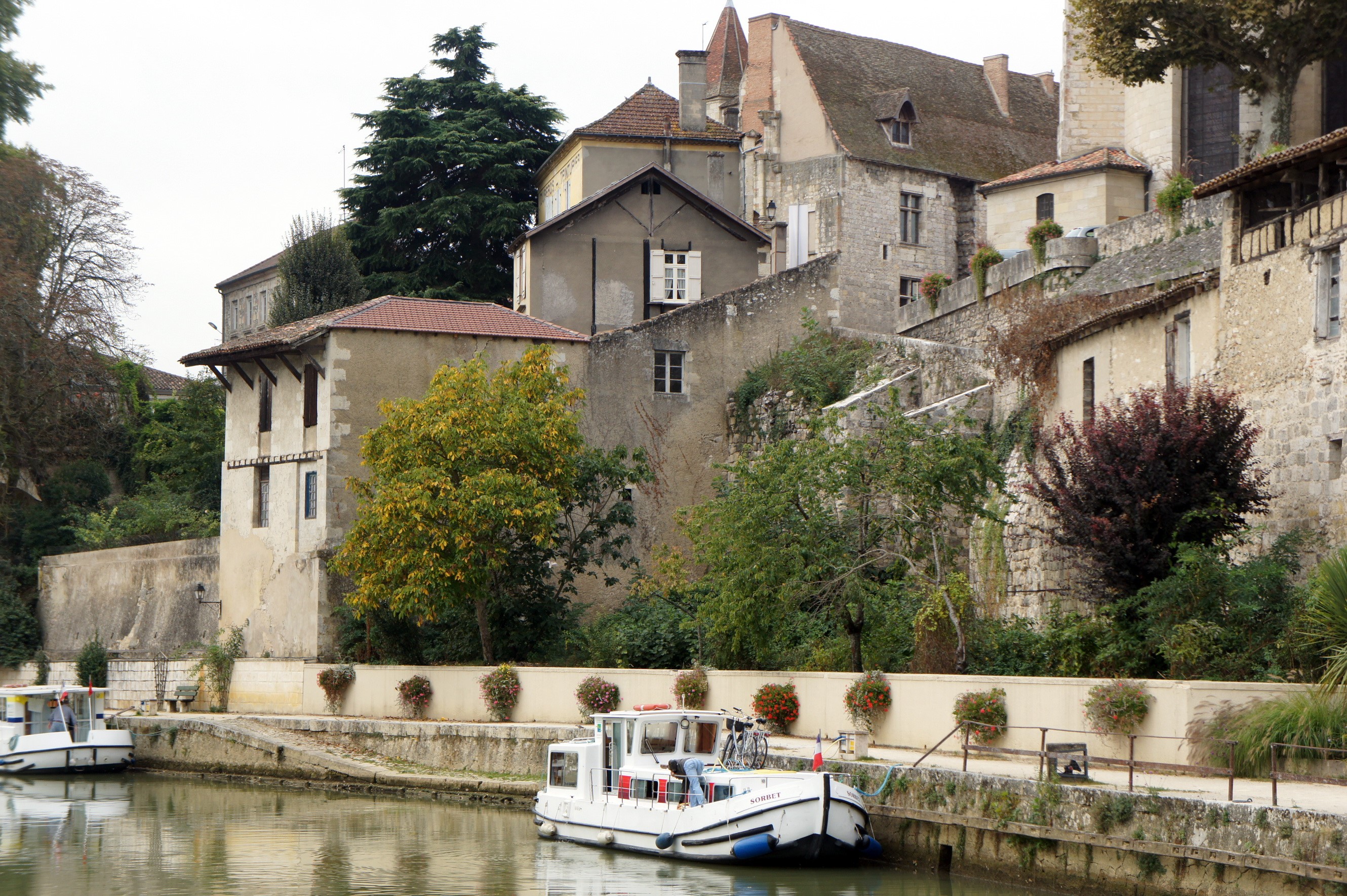 Boats docked along a canal in a French town with stone buildings HD Wallpaper