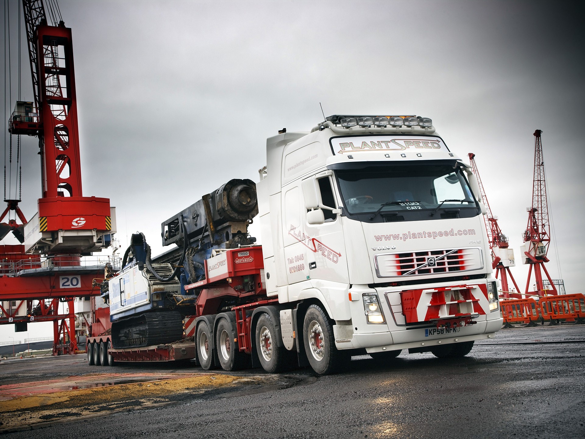 Volvo truck carrying heavy machinery at a port HD Wallpaper