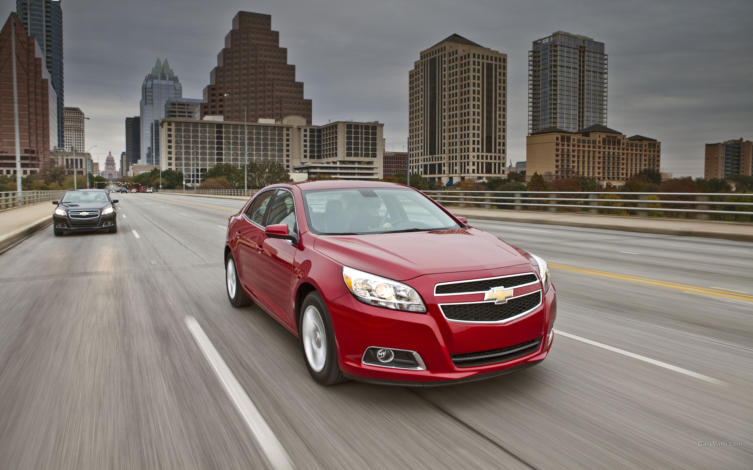Red Chevrolet Malibu driving on a city bridge HD Wallpaper