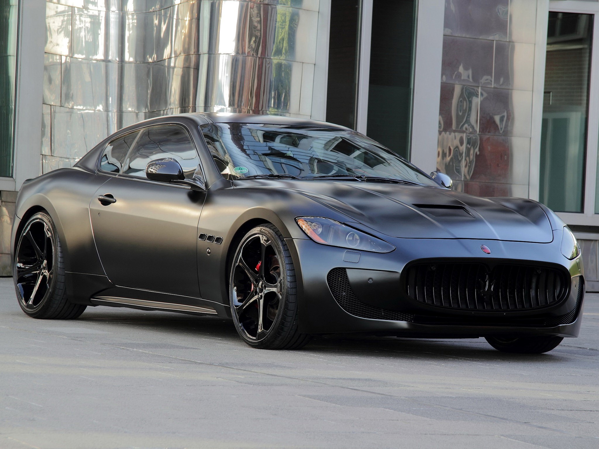 Matte black Maserati GranTurismo parked outside a modern building HD Wallpaper