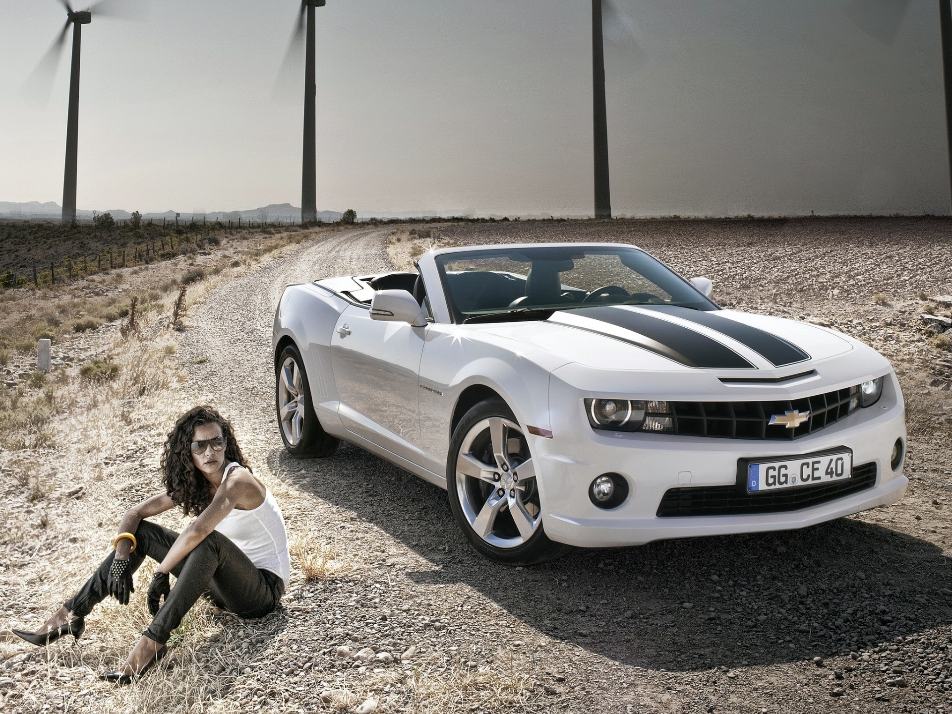 Woman and Chevrolet Camaro Convertible on a dirt road with wind turbines HD Wallpaper