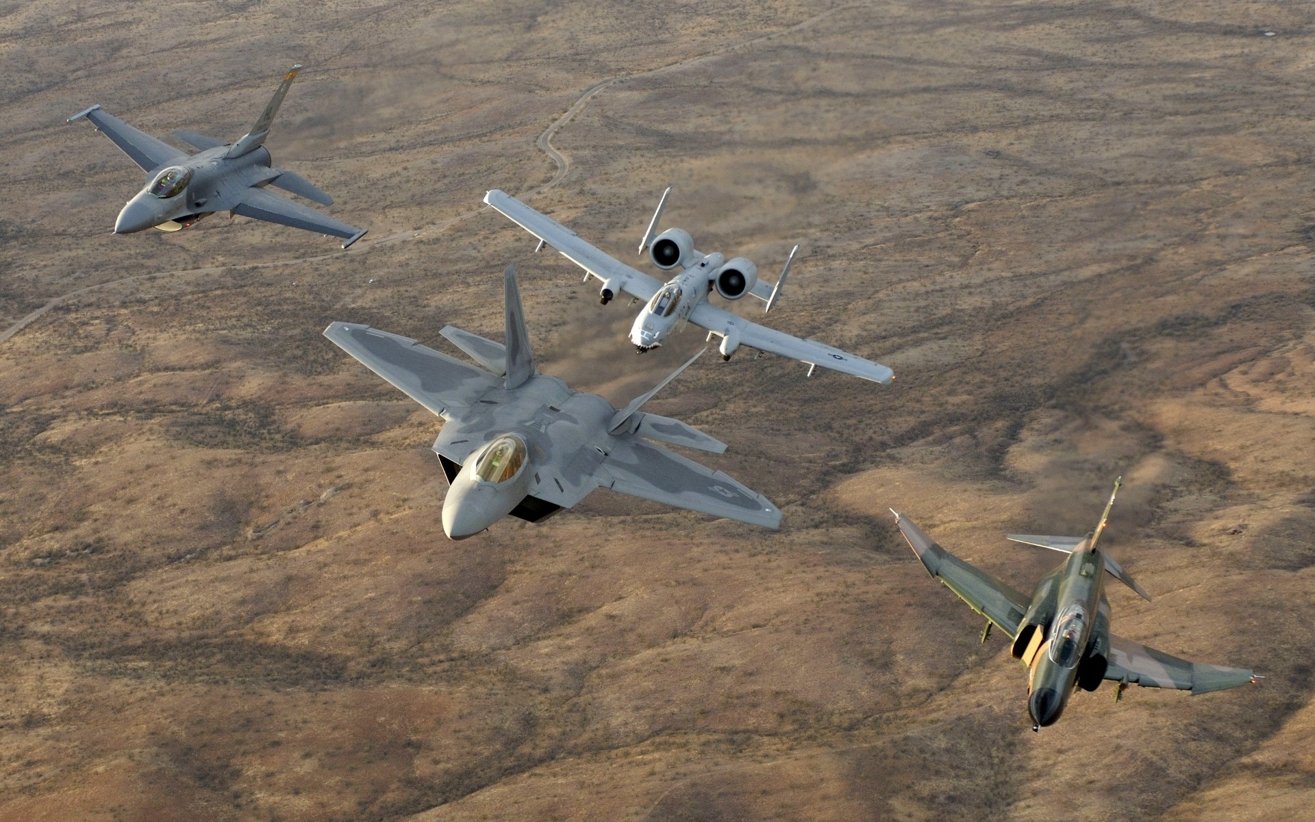 Four military jets flying over desert terrain HD Wallpaper