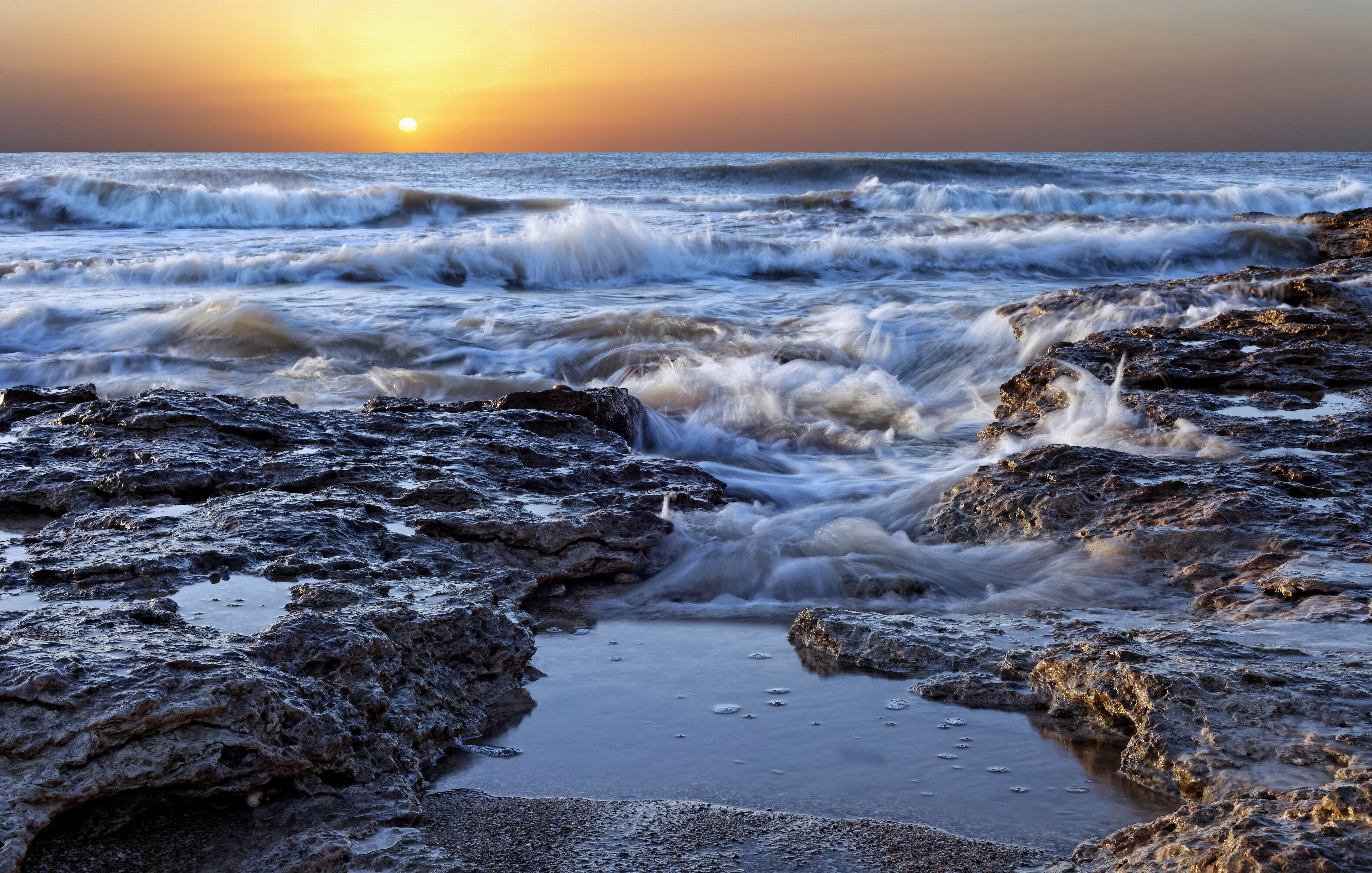Sunset over the ocean with waves crashing on rocks HD Wallpaper