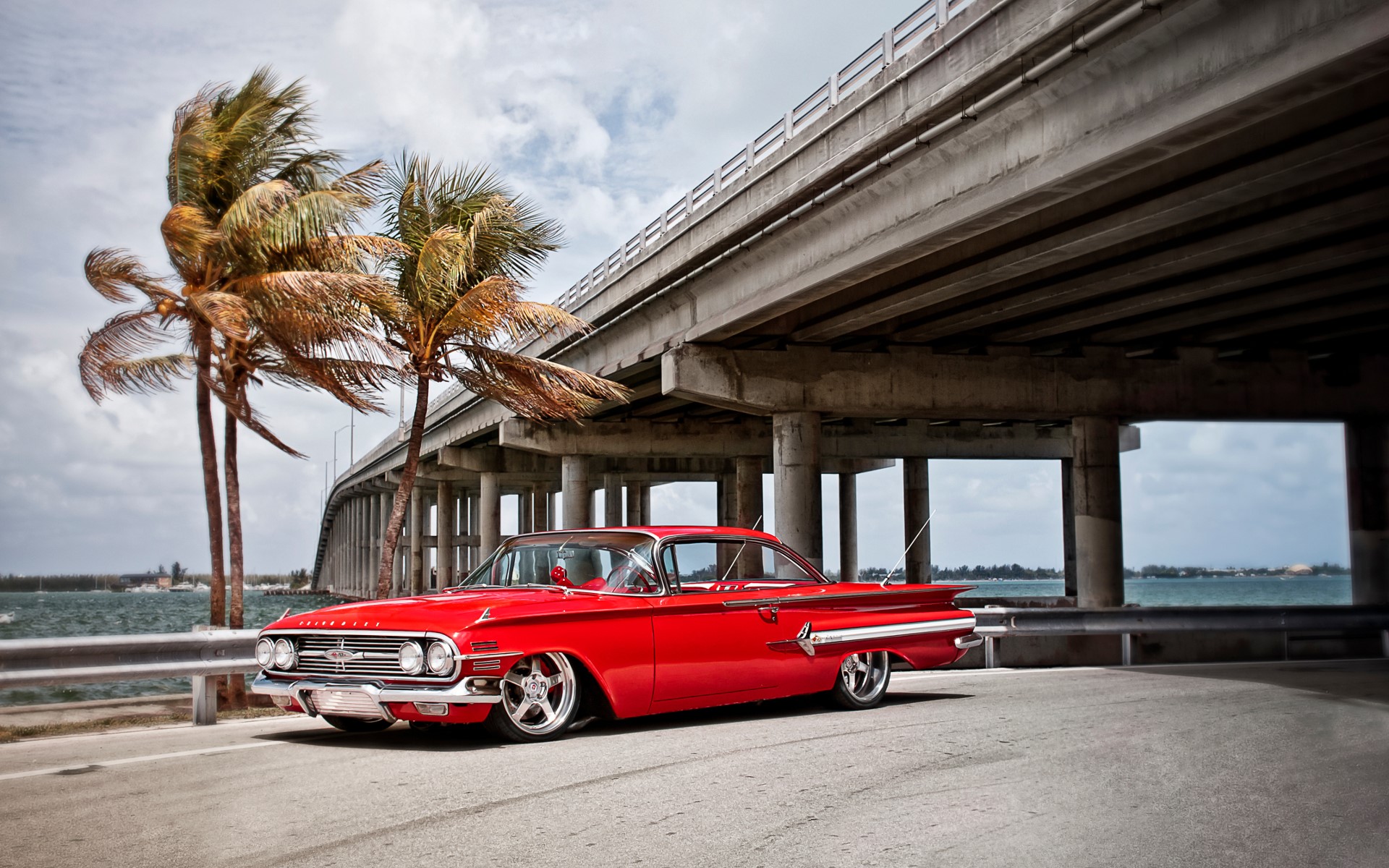 Red Chevrolet parked under a bridge with palm trees HD Wallpaper