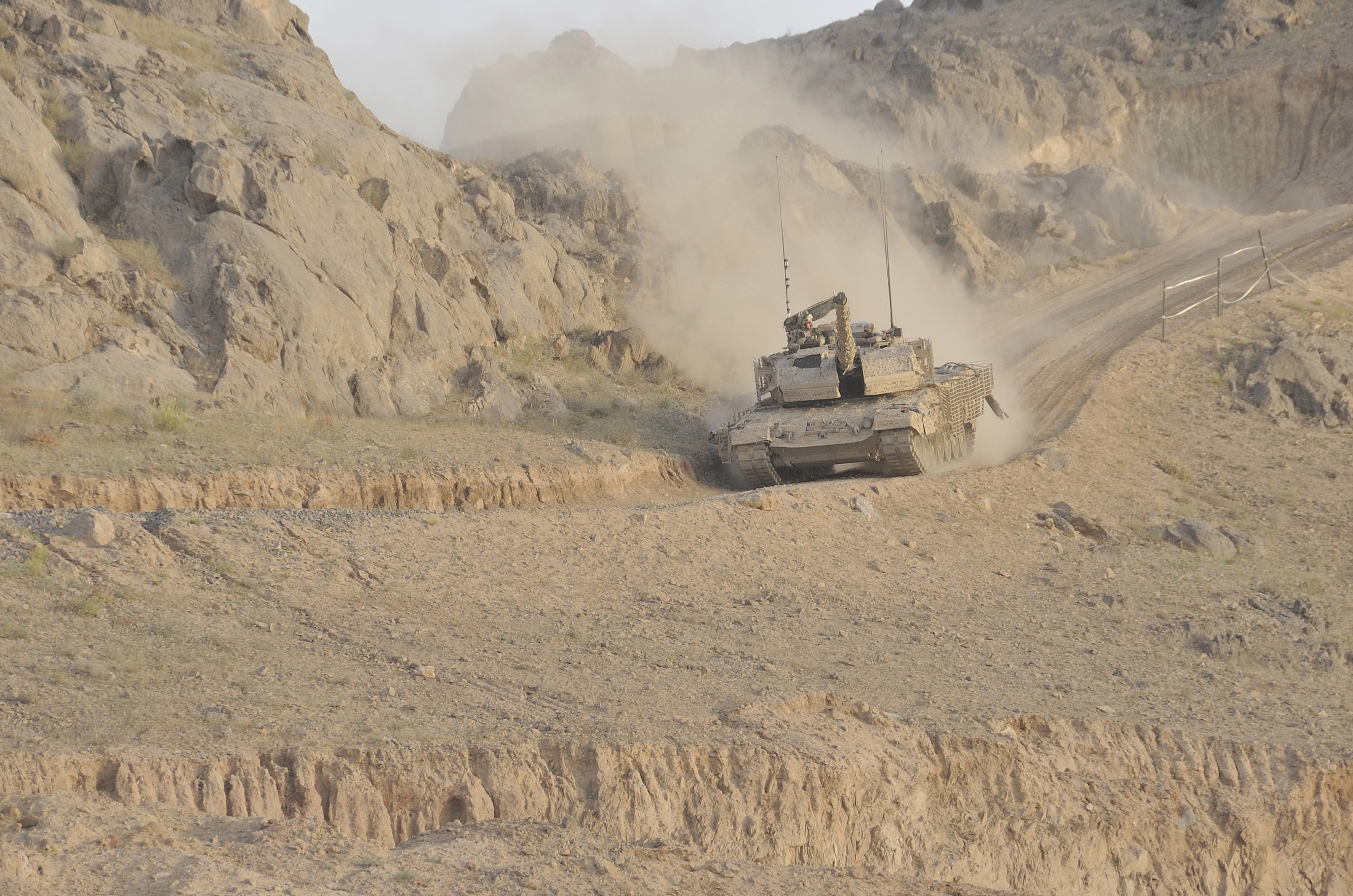 Tank driving on a dusty mountain road HD Wallpaper