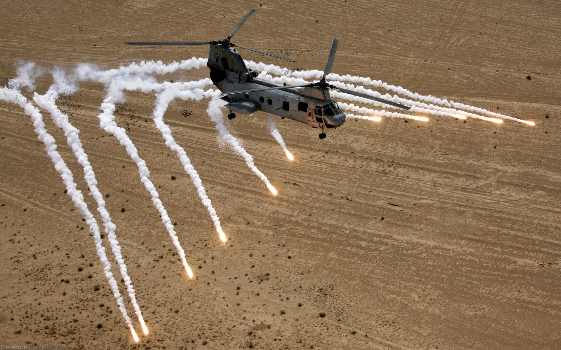 Helicopter deploying flares over desert terrain HD Wallpaper