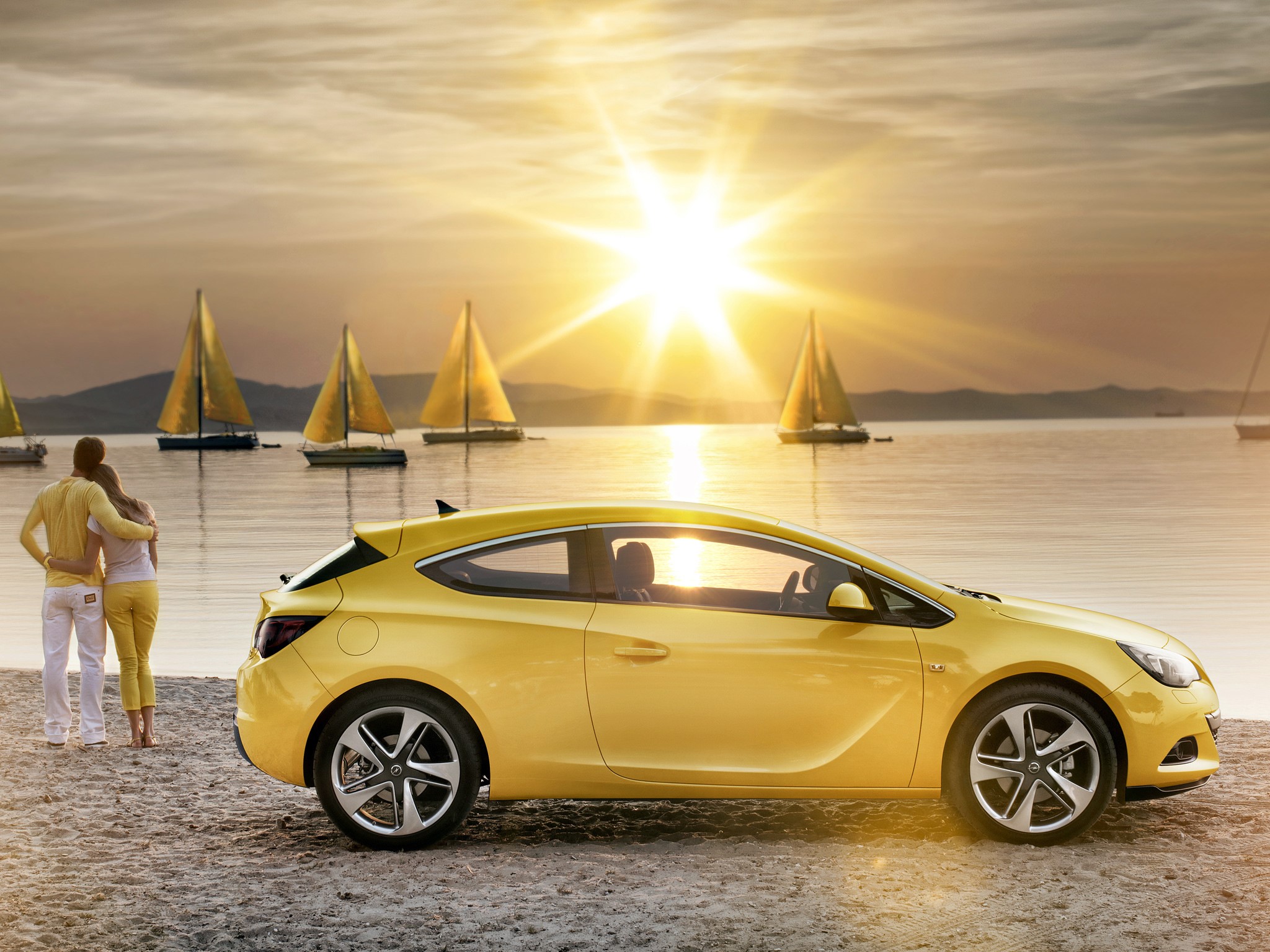 Yellow Opel Astra on a beach with sailboats at sunset HD Wallpaper