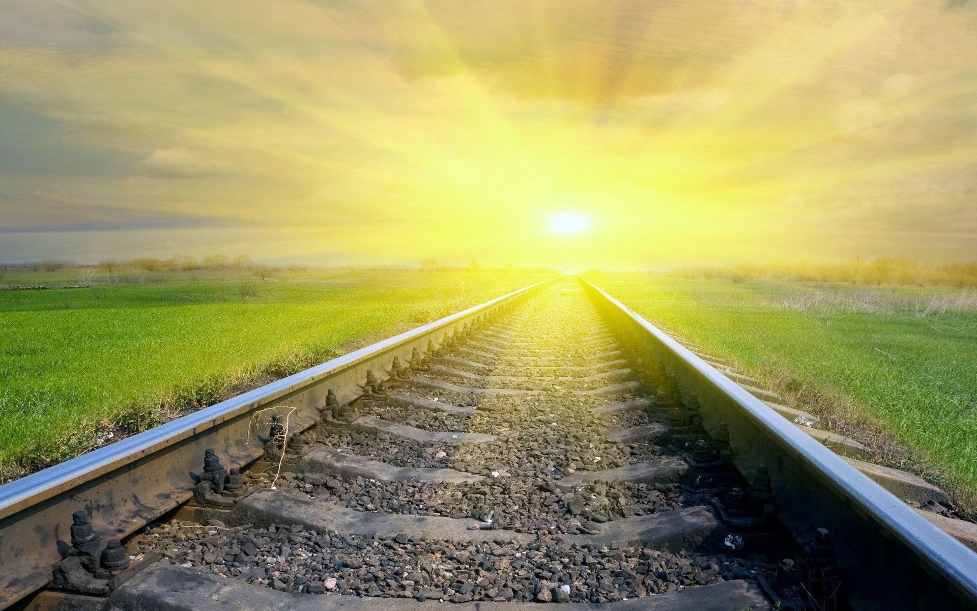 Train tracks leading to a bright sun over a green field HD Wallpaper